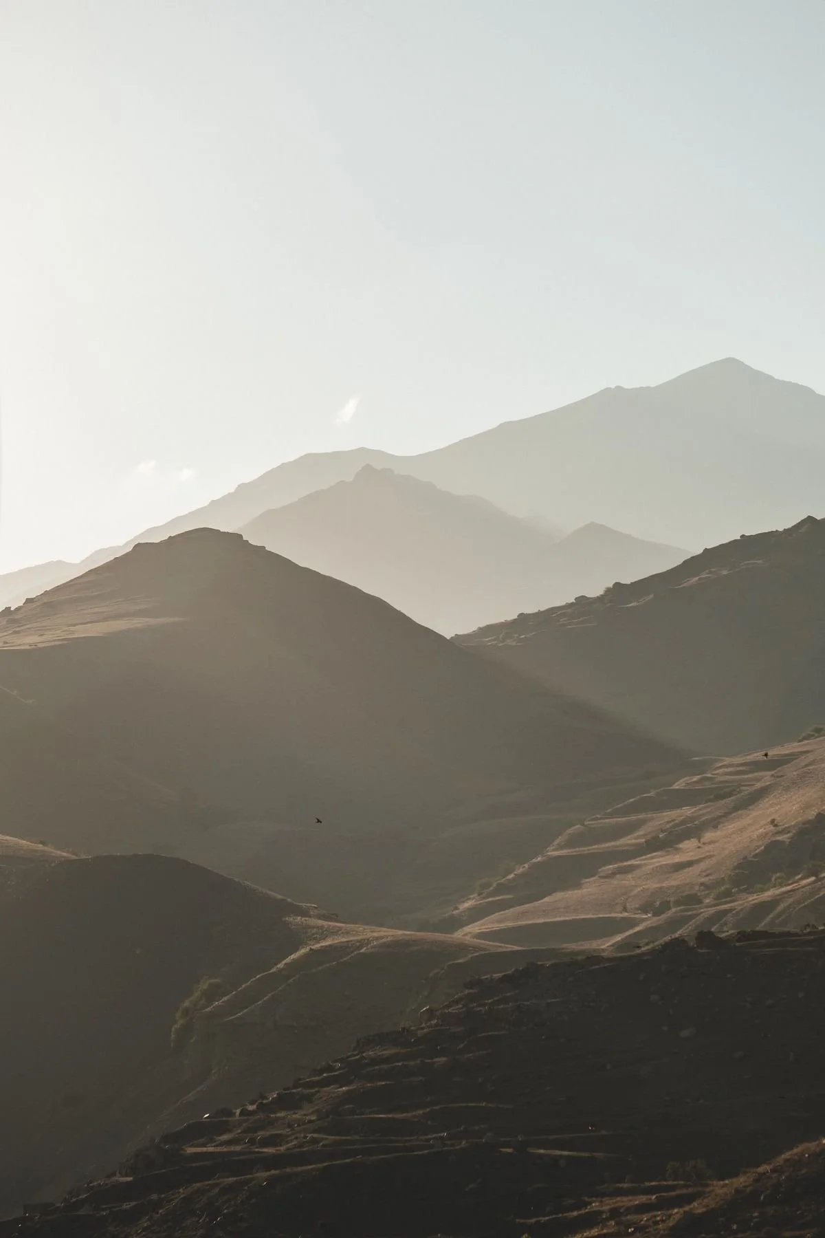 Mountain landscape with multiple layers of mountains in the distance, under a pale sky.
