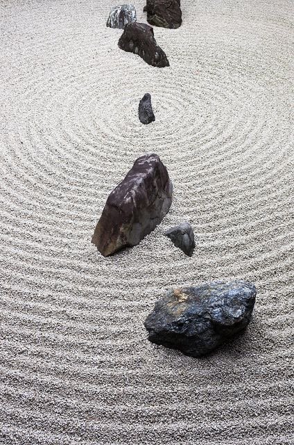A Zen rock garden with several large dark stones arranged in a pattern on raked white gravel.