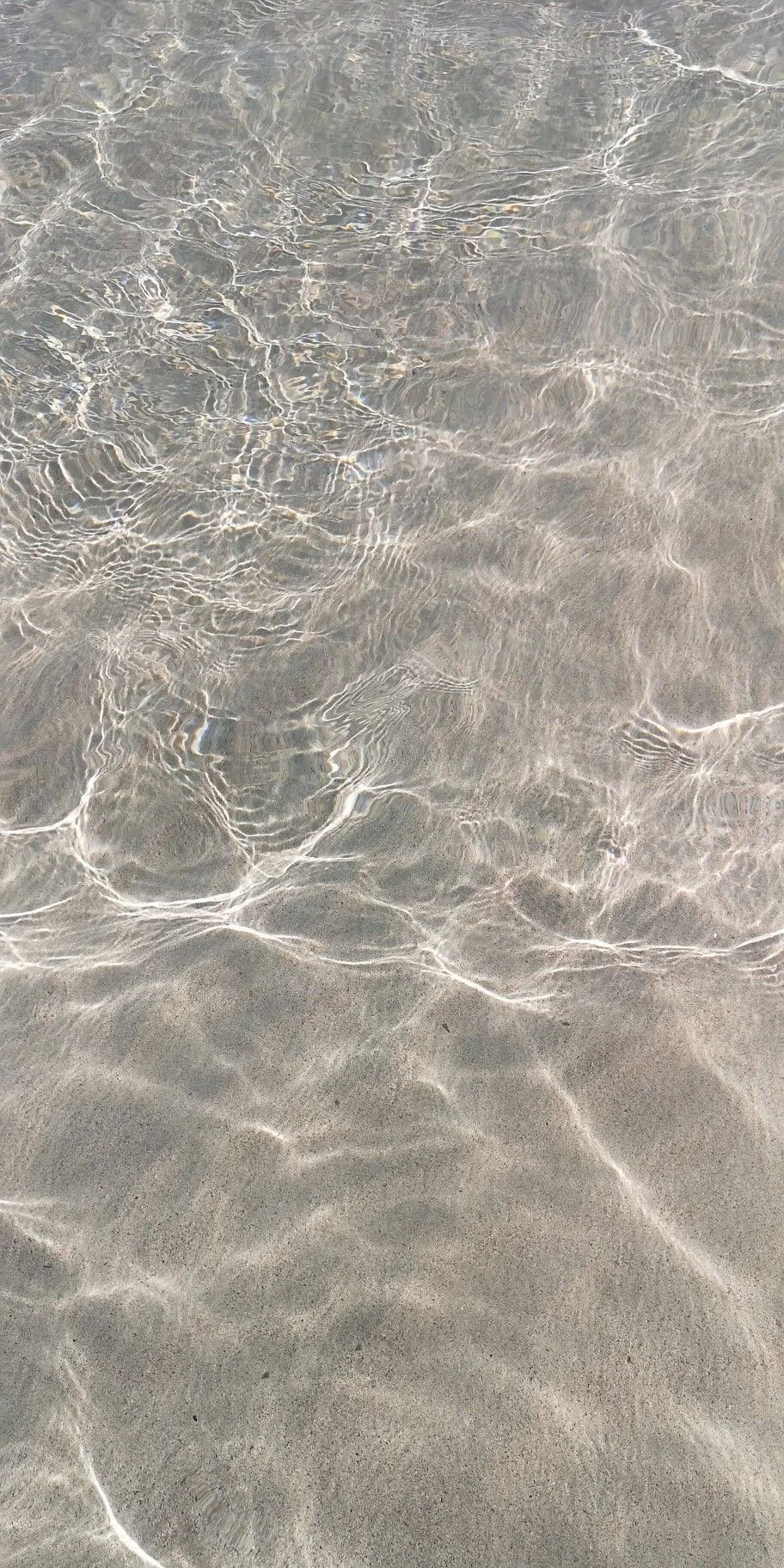 Clear shallow water over sandy beach with light reflections and ripples.