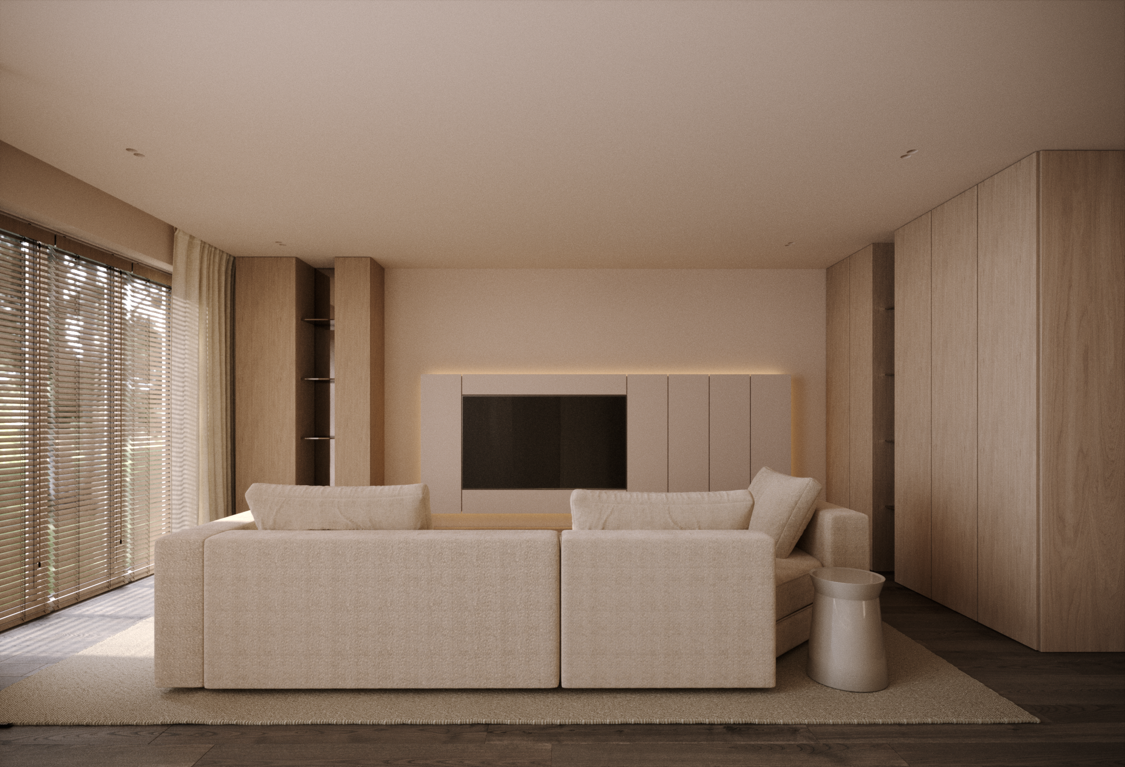 A modern living room with beige fabric sofas facing a flat-screen TV mounted on a white wall, with built-in wooden shelves on either side, and large windows with wooden blinds.