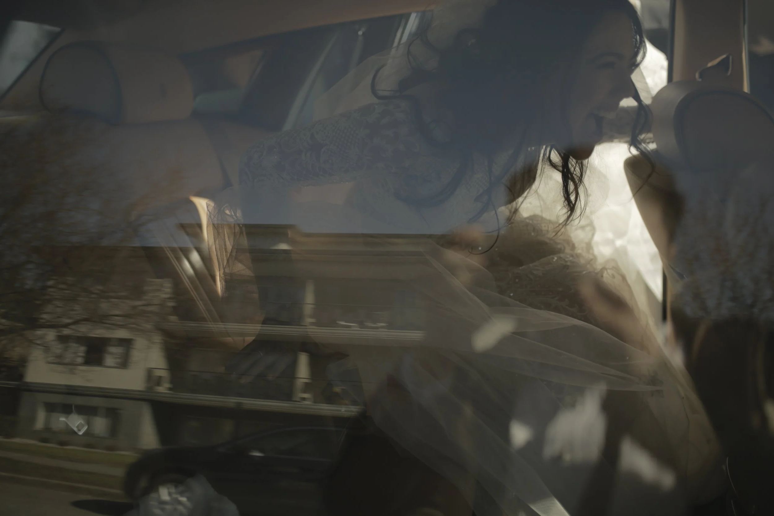 Woman smiling and leaning into the front seat of a car, with reflections of houses and trees on the window.