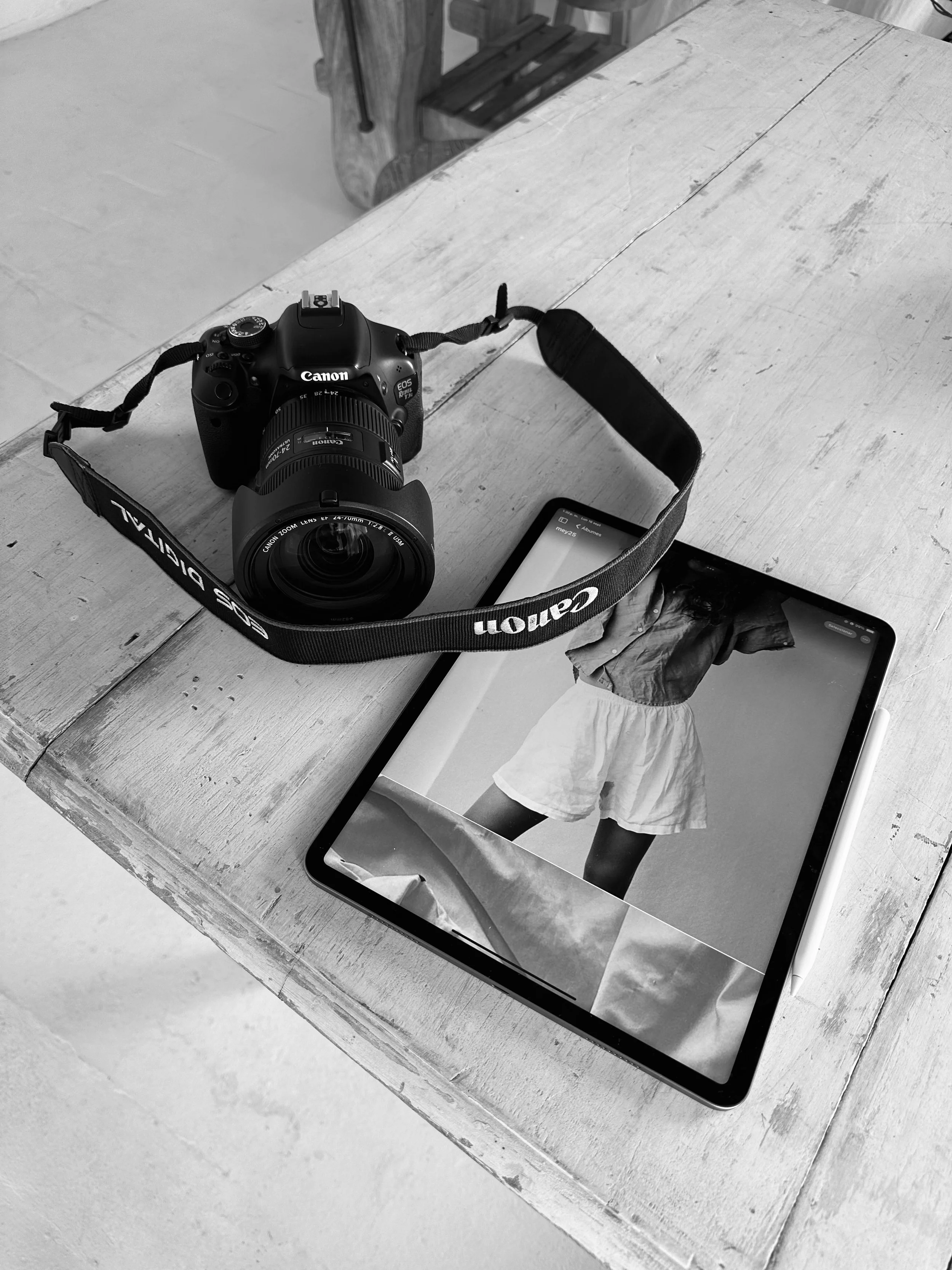 A Canon camera and a tablet displaying a photo of a person in shorts and a top on a wooden table.