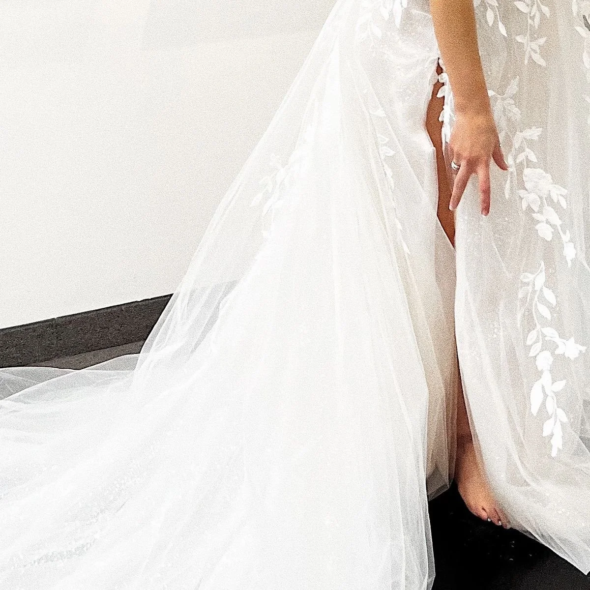 Close-up of a bride lifting her wedding dress to show her leg and foot, wearing a wedding gown with floral embroidery.