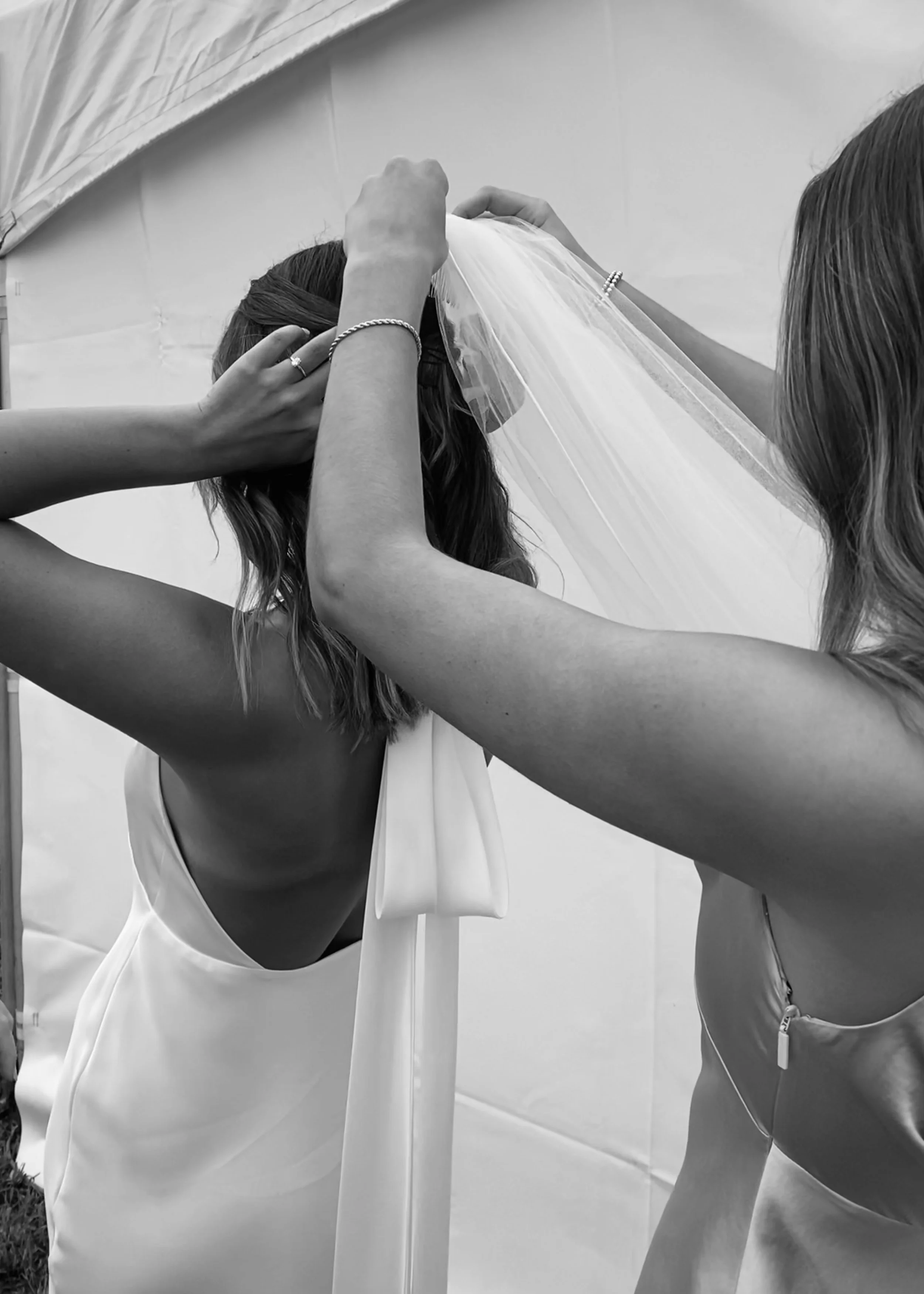Two women fitting a bride's veil onto her head during wedding preparations