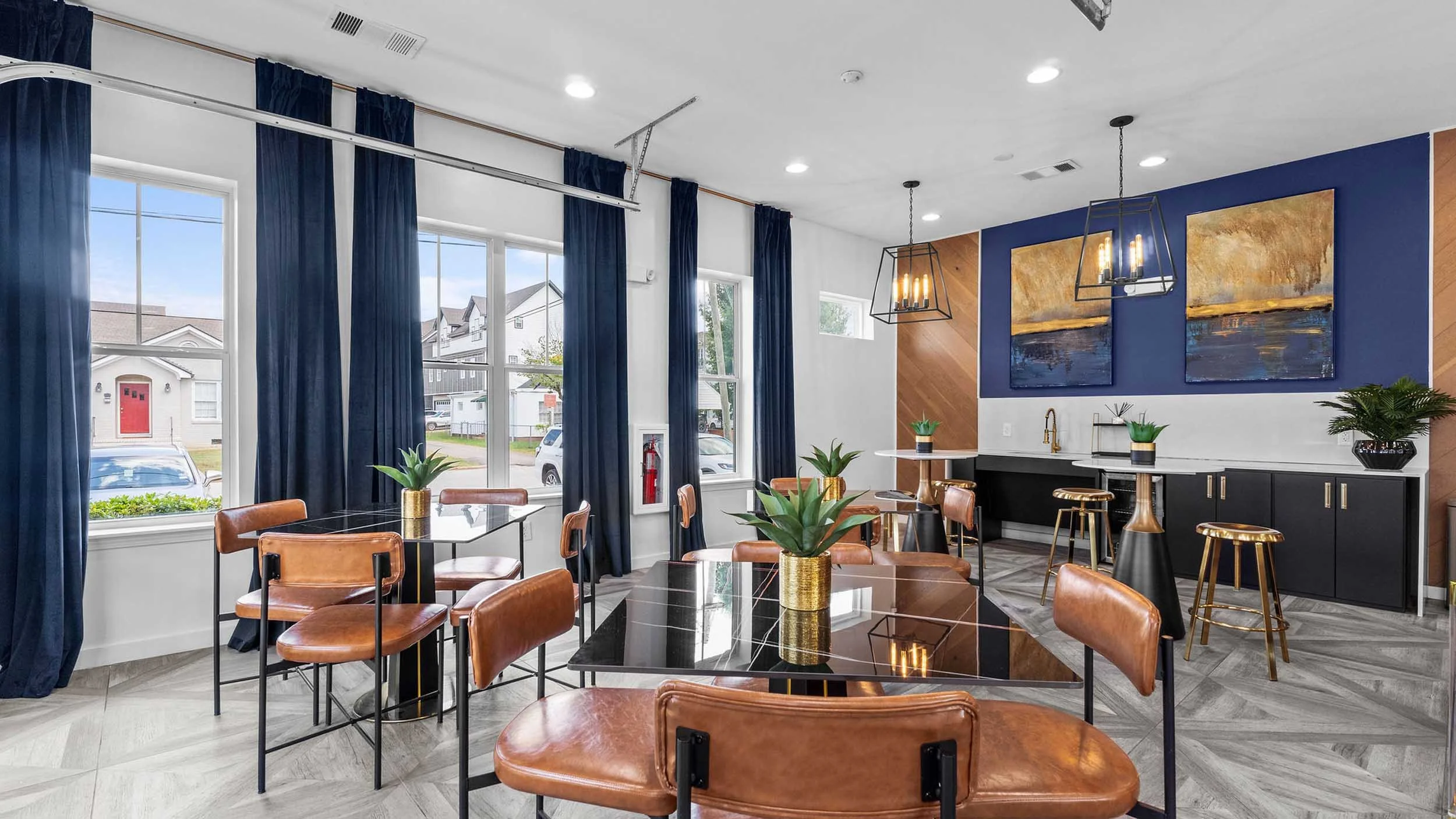 Modern resident lounge with large windows, navy blue curtains, black tables with leather chairs, and decorative plants.