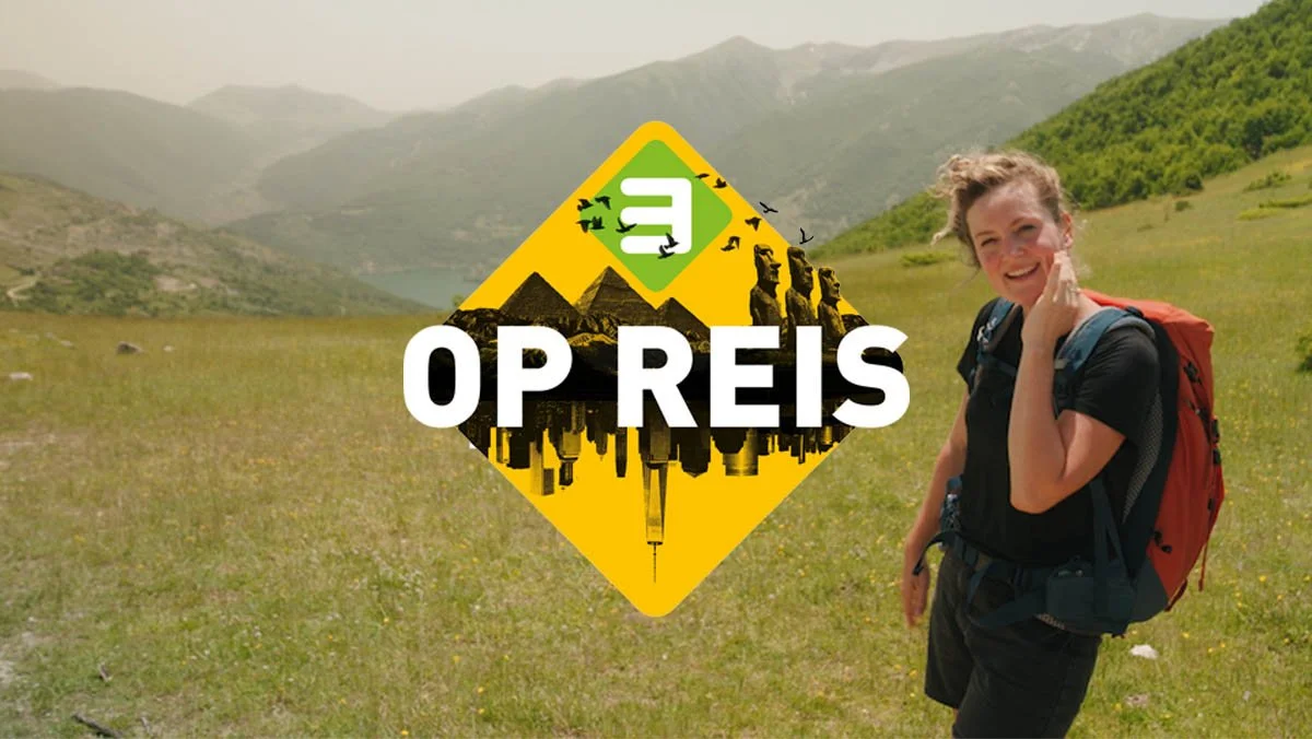 Vrouw met een rugzak die wandelt in een groen landschap met bergen op de achtergrond en een logo met de tekst '3 Op Reis'.
