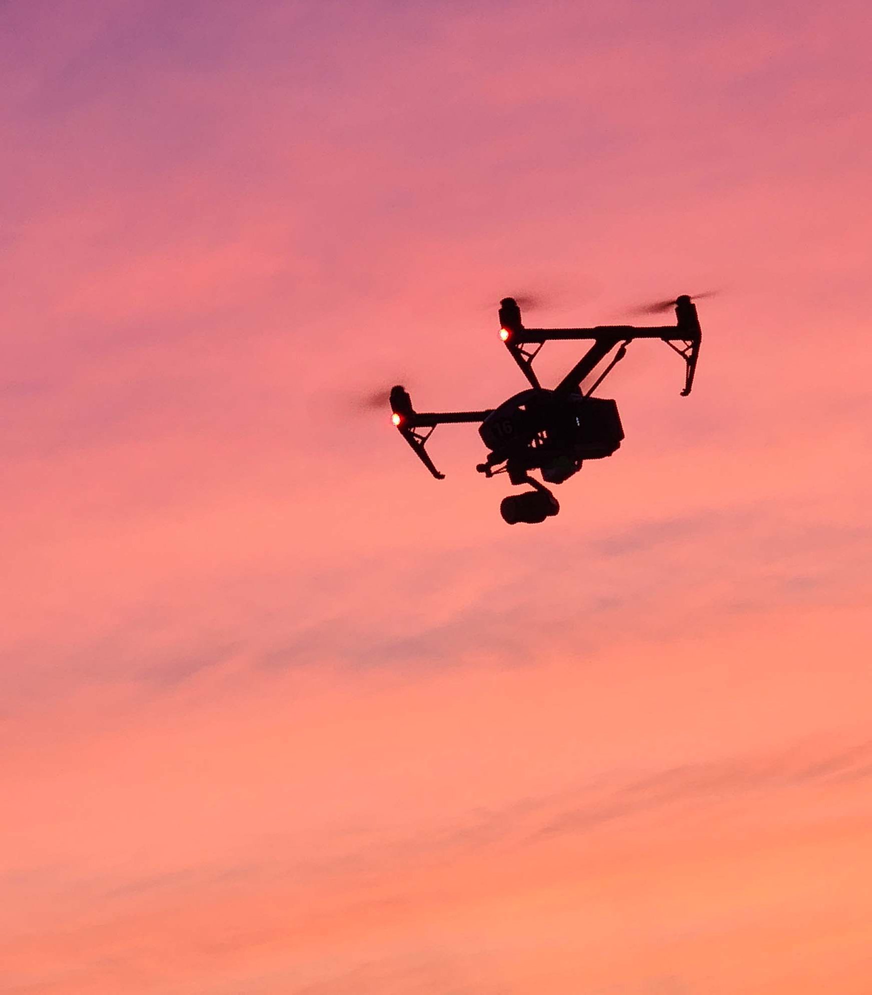 Drone soaring against the sunset sky, capturing aerial views.