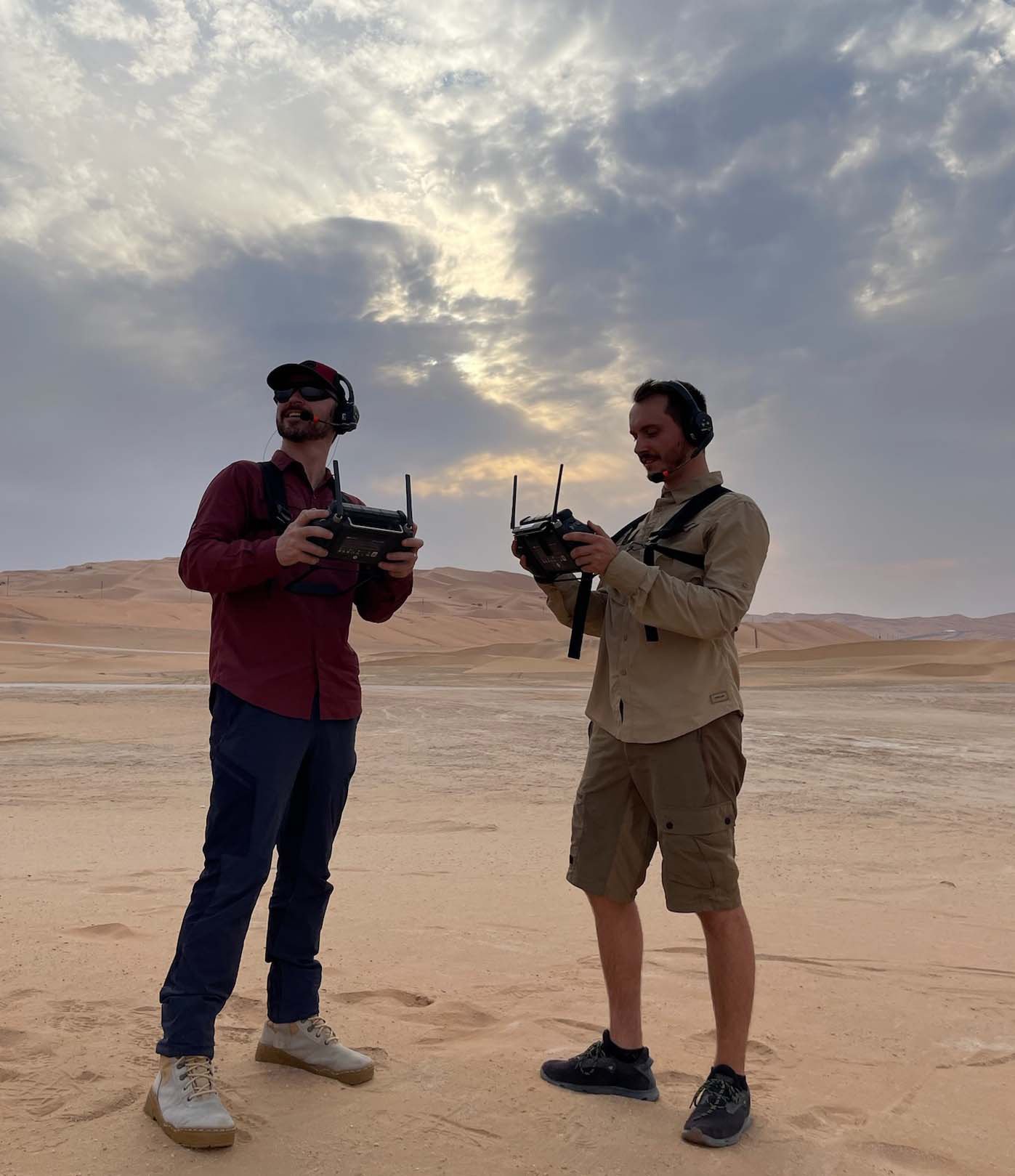  Two drone operators with control panels overseeing a desert shoot, coordinating aerial filming operations. 