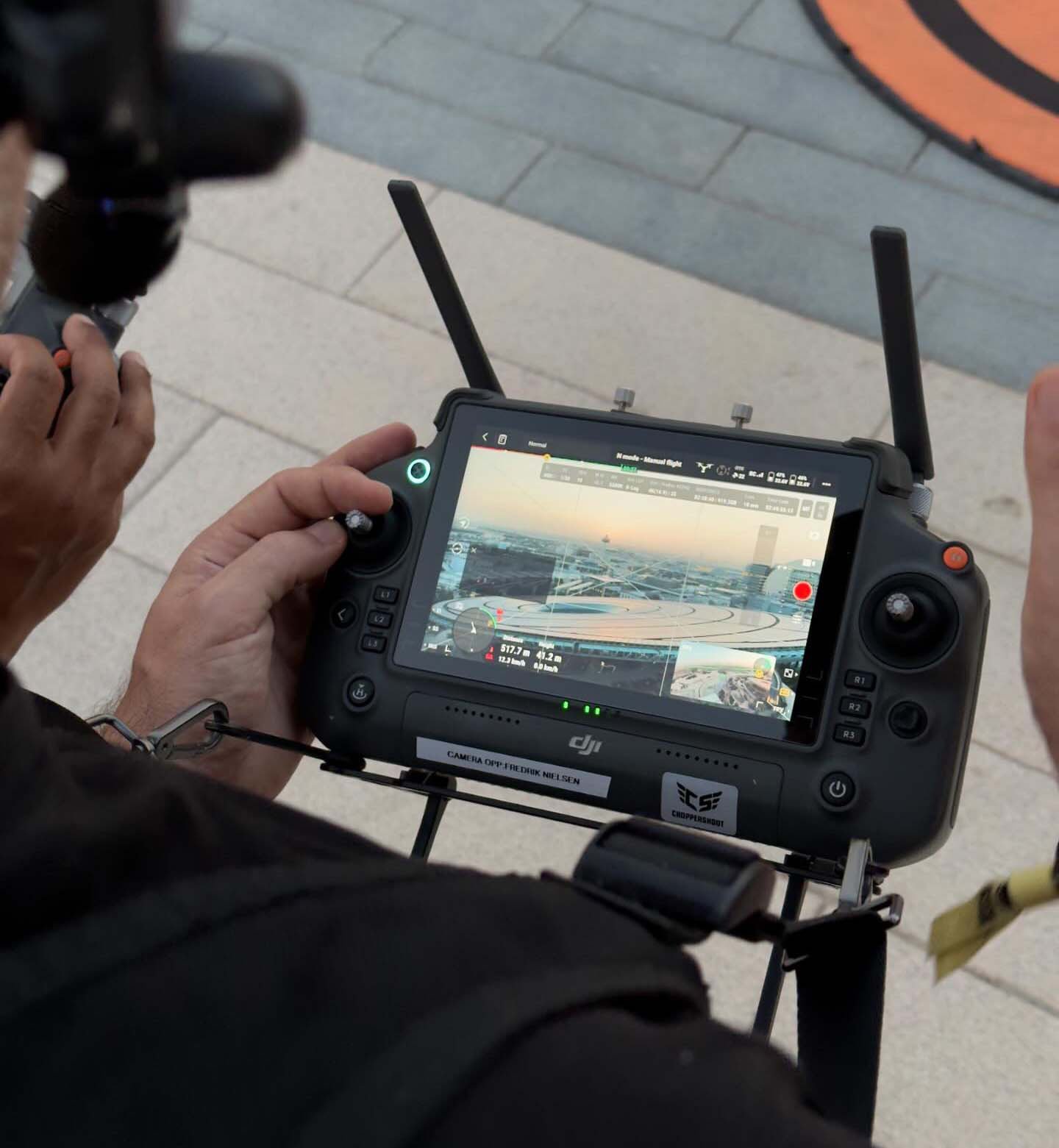 Operador de dron con mandos a distancia en la mano, supervisando una sesión de filmación.