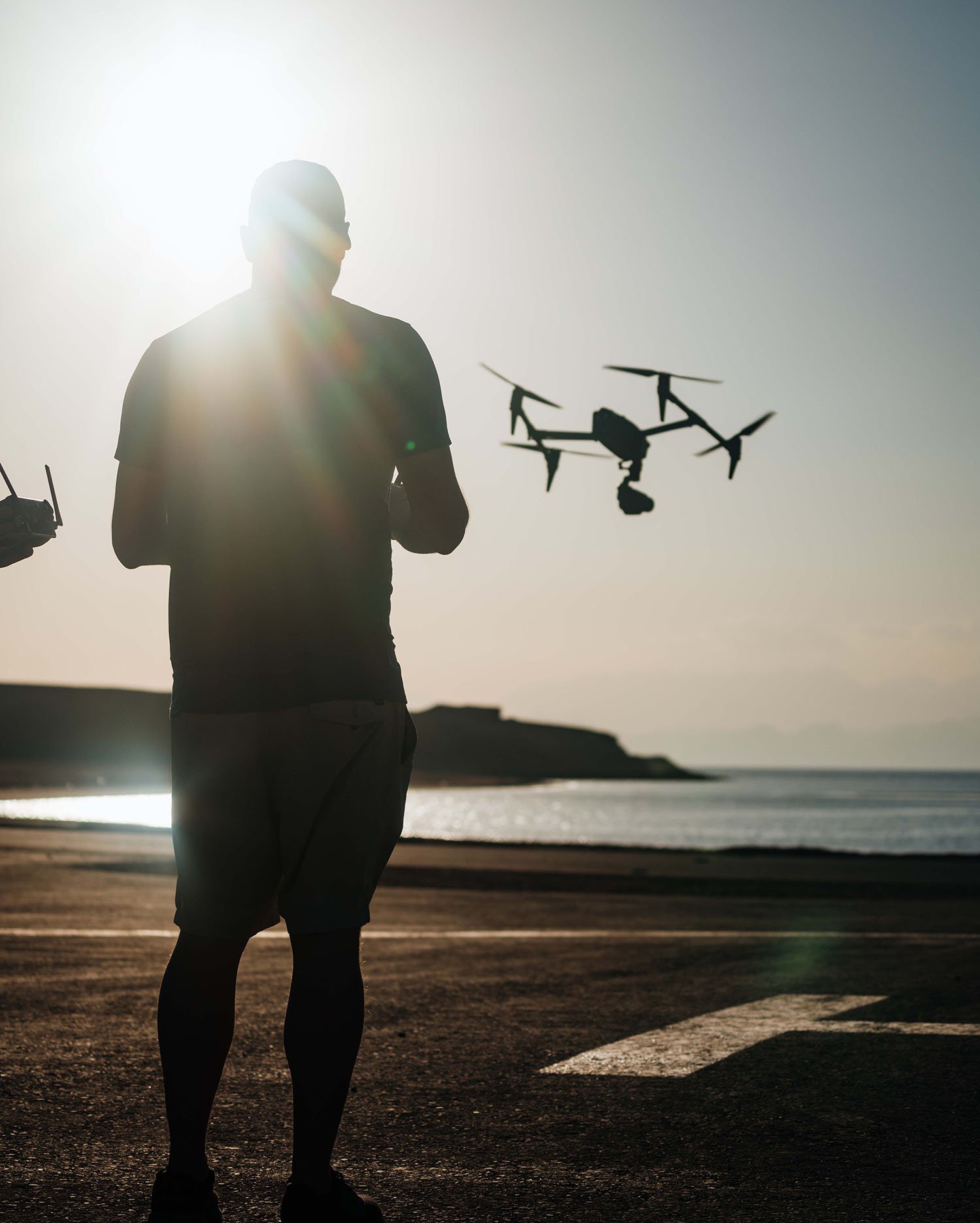  Operador de dron pilotando un dron sobre una playa de arena, captando imágenes aéreas de la costa. 