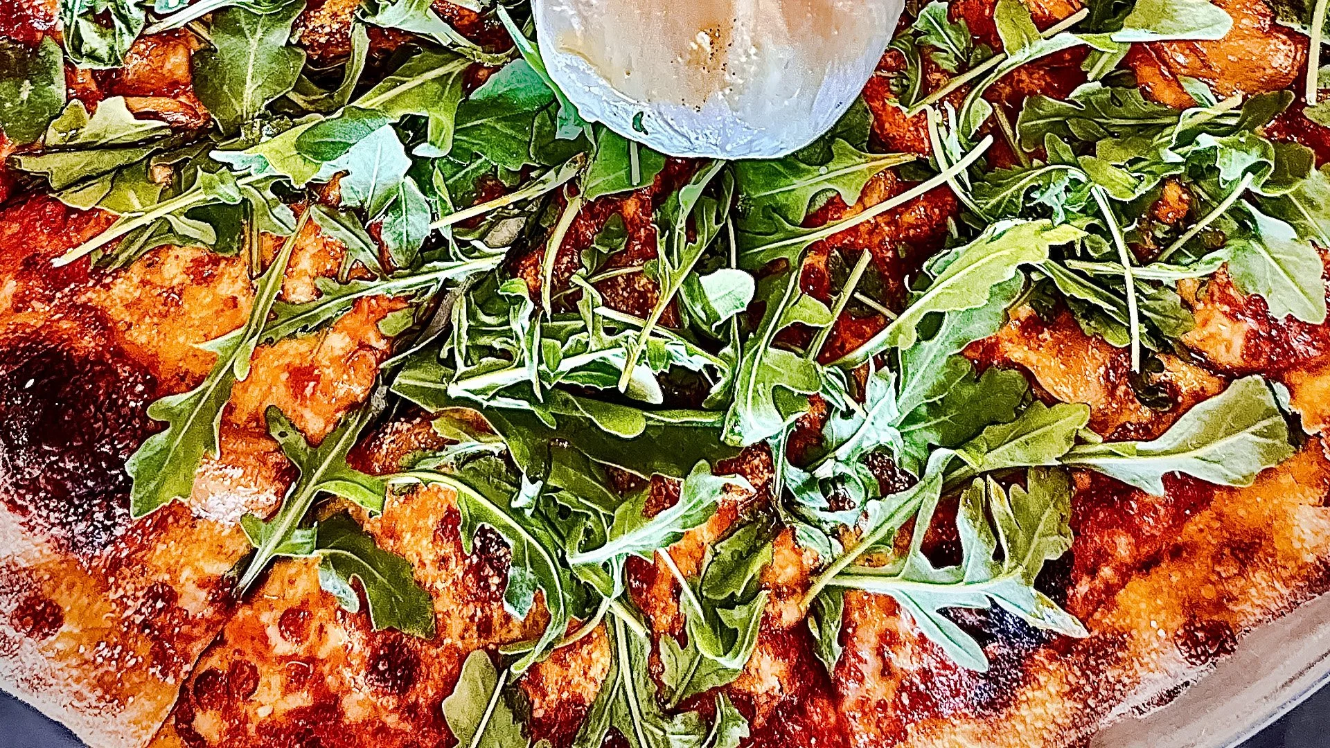 Pizza with a topping of arugula leaves and melted cheese.