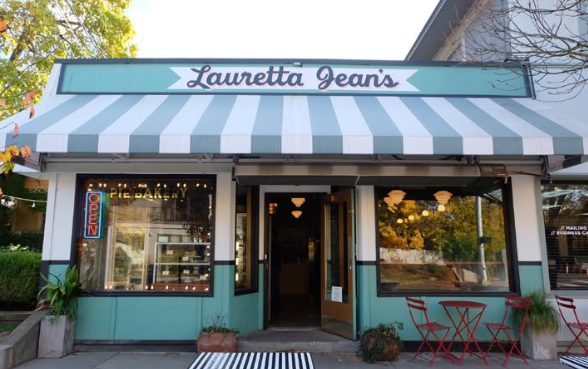 Exterior of Lauretta Jean's bakery with a striped awning, open sign, and outdoor seating with red chairs and tables.
