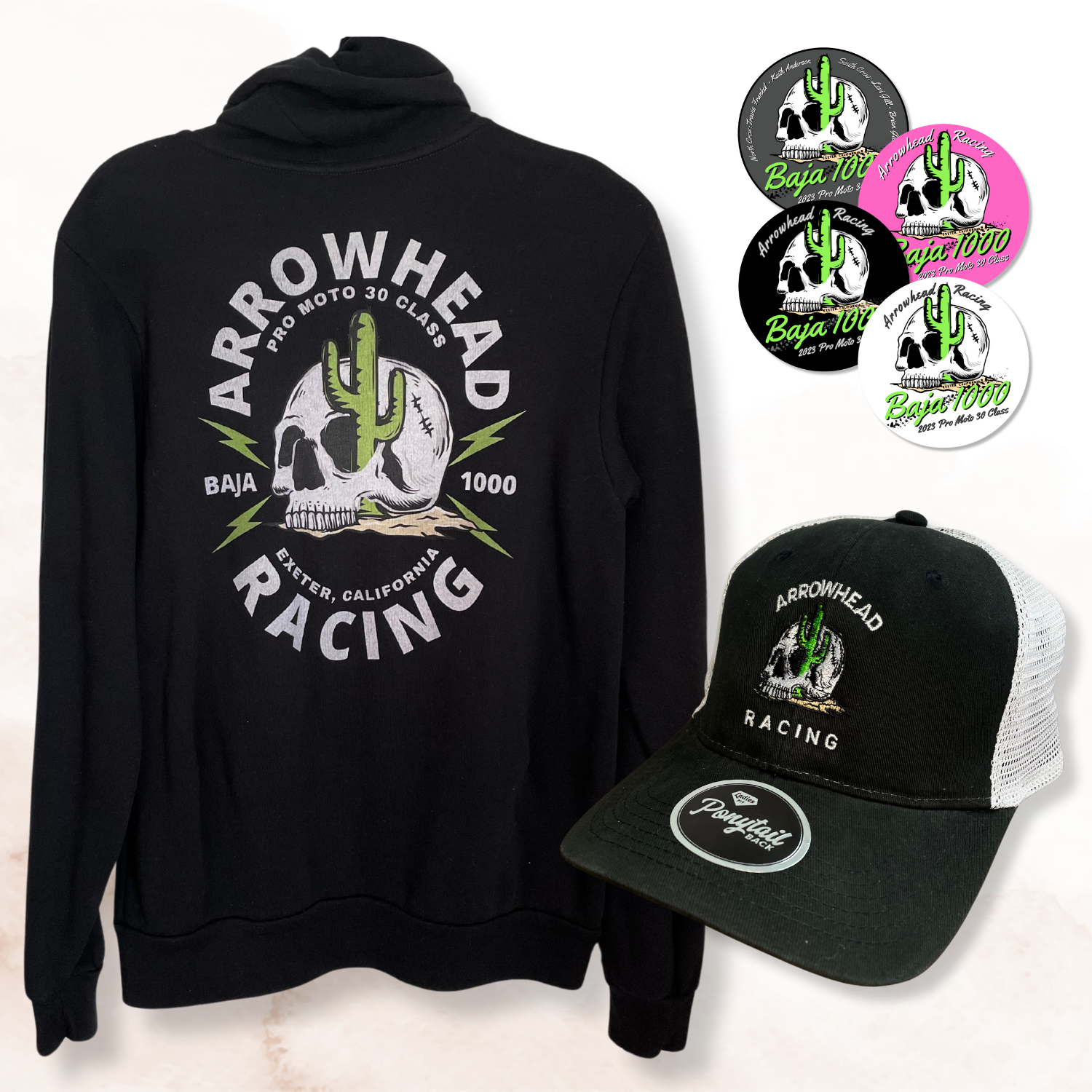 Black hoodie and trucker hat with Arrowhead Racing logo, featuring a skull and cactus design, alongside circular stickers with similar motifs.