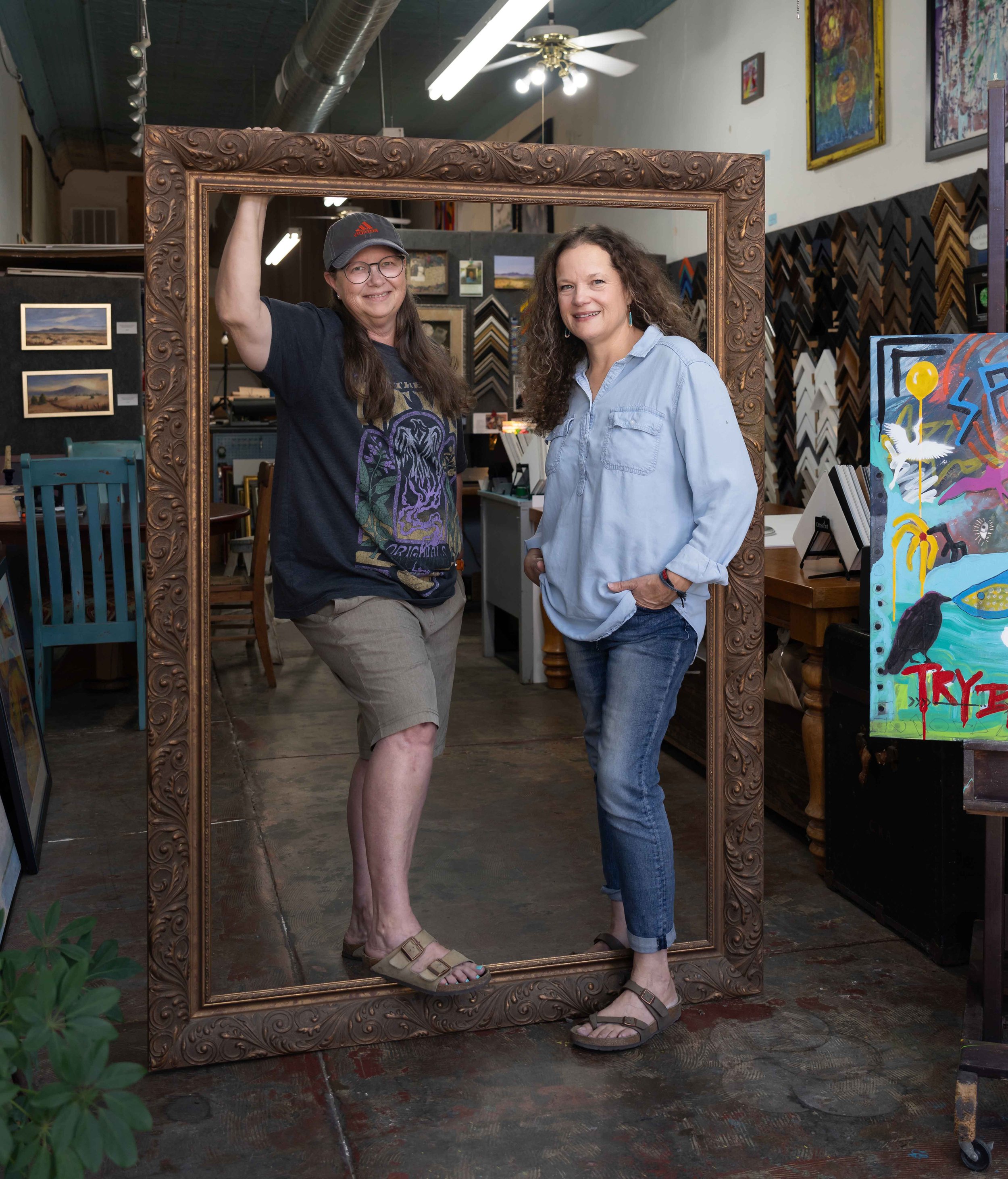 Lively portrait of two art framers inside a large portrait frame. 