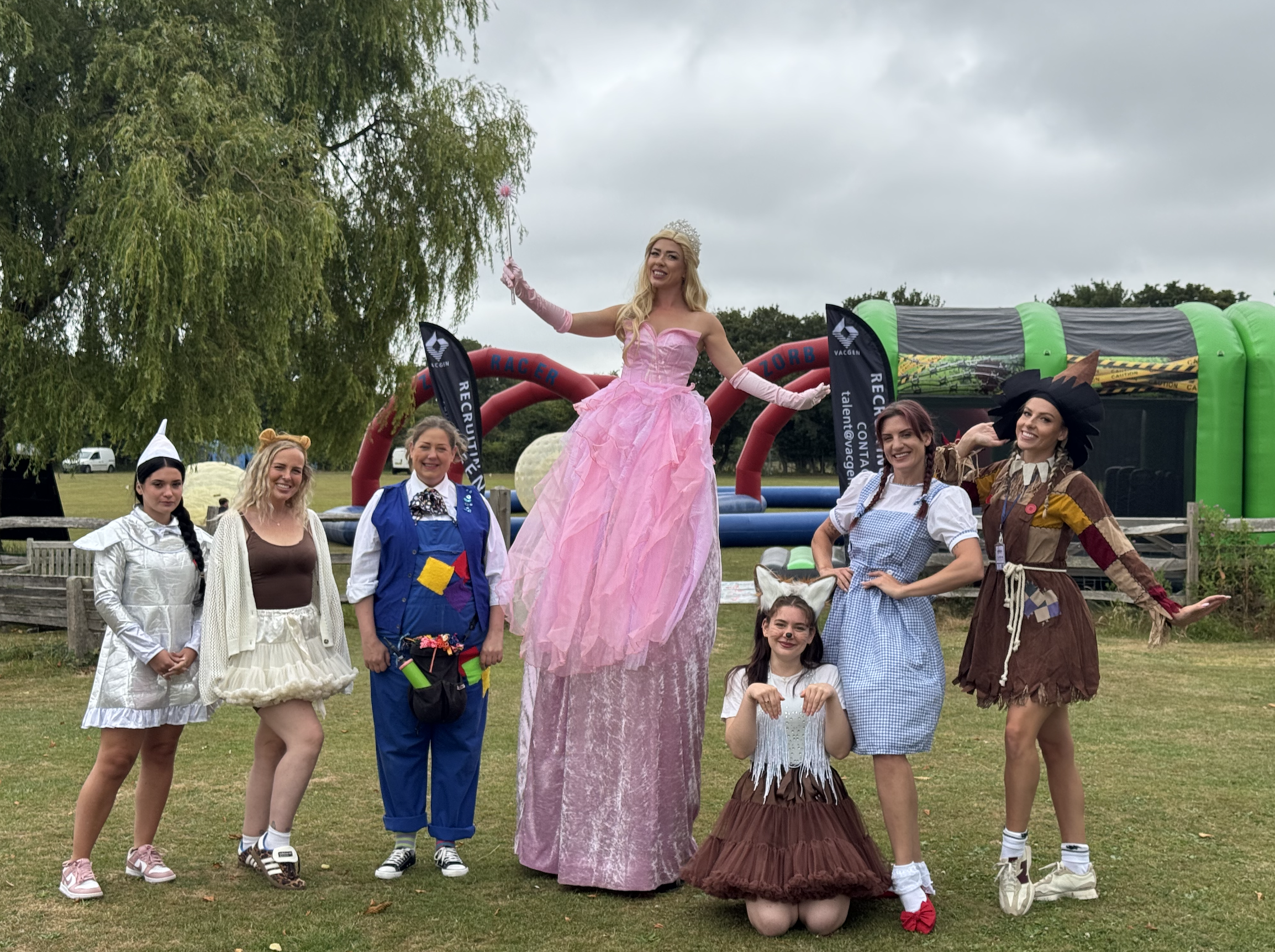 stilt walking Glinda with tin man, lion, munchkin, toto, dorothy and scarecrow performers