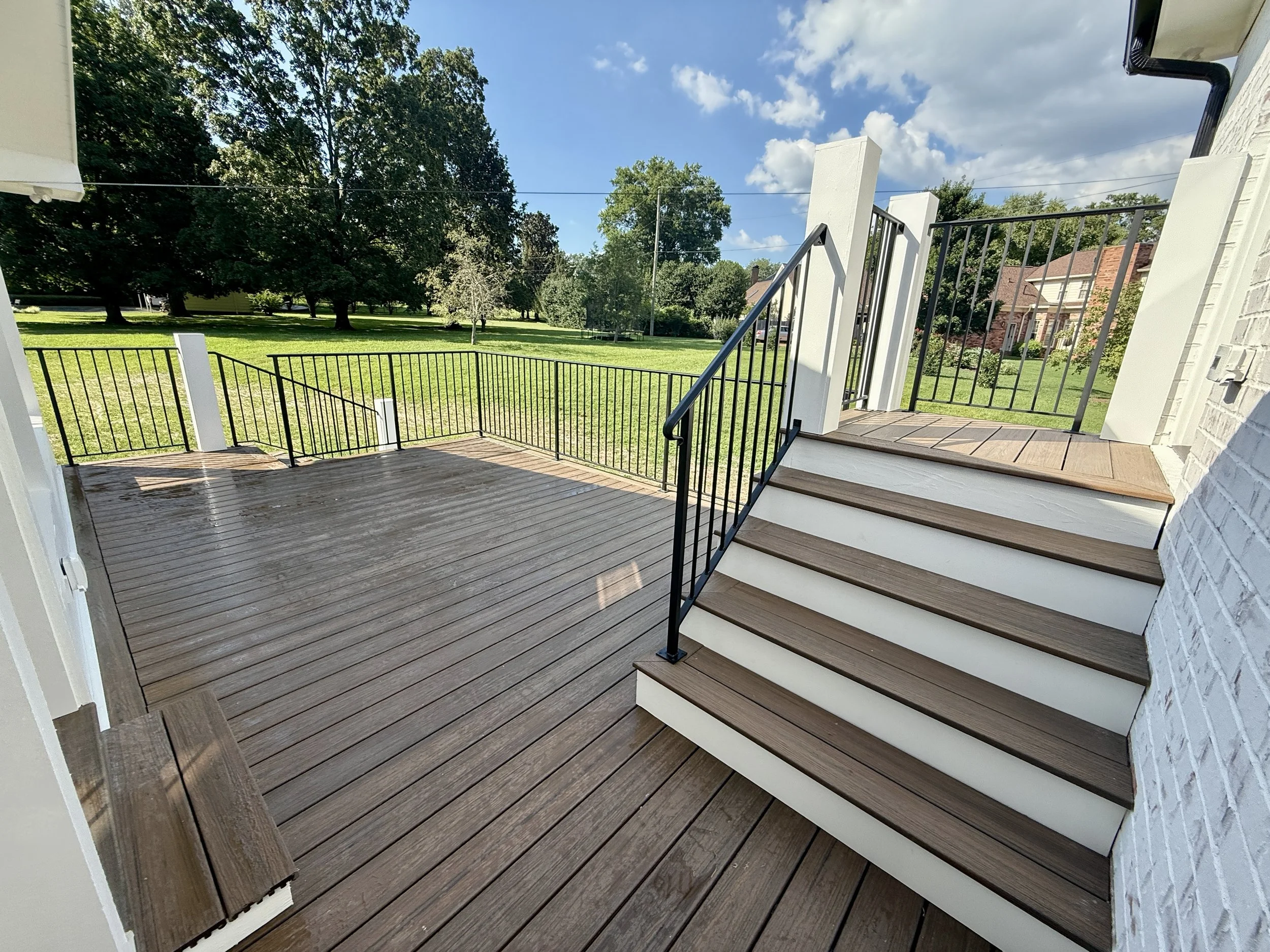 Uncovered composite deck with black metal railing and stairs connecting the main home, screened porch, and new detached accessory dwelling unit.