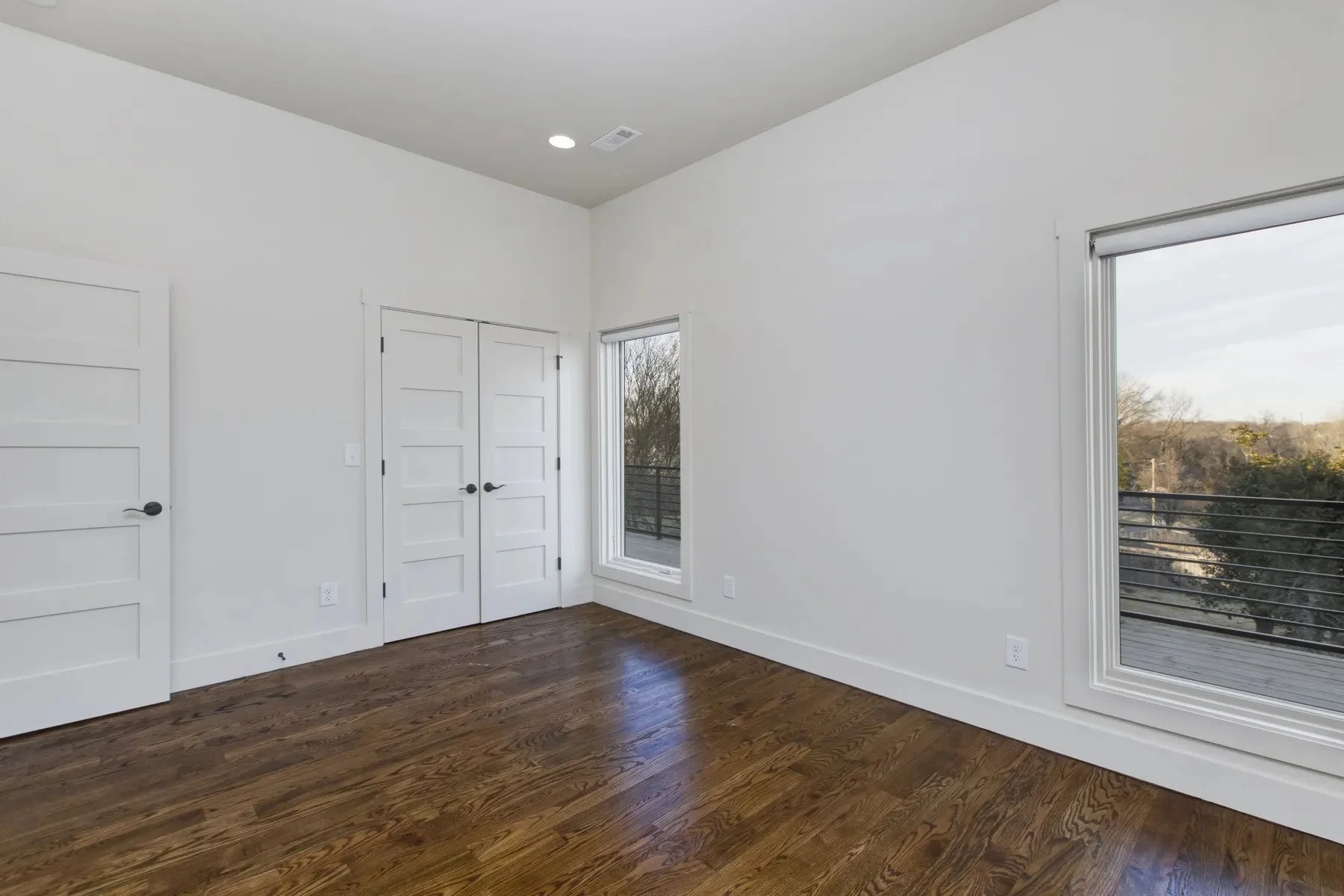 Bedroom with hardwood floors, double doors, and large windows providing natural light in a newly constructed duplex.