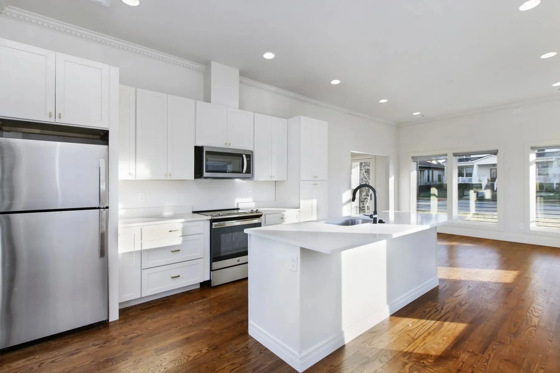 Wide-angle view of a white kitchen with a center island, hardwood floors, and natural light in a newly built duplex residence.