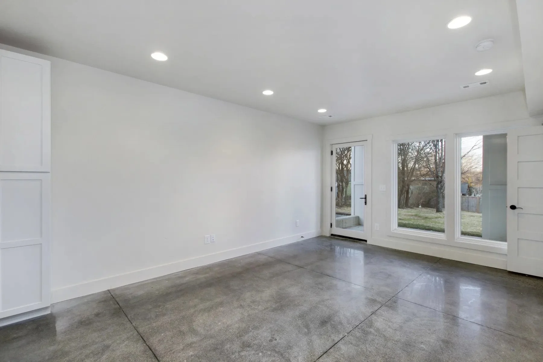 Lower-level living space with polished concrete floors, recessed lighting, and backyard access in a duplex rental home.