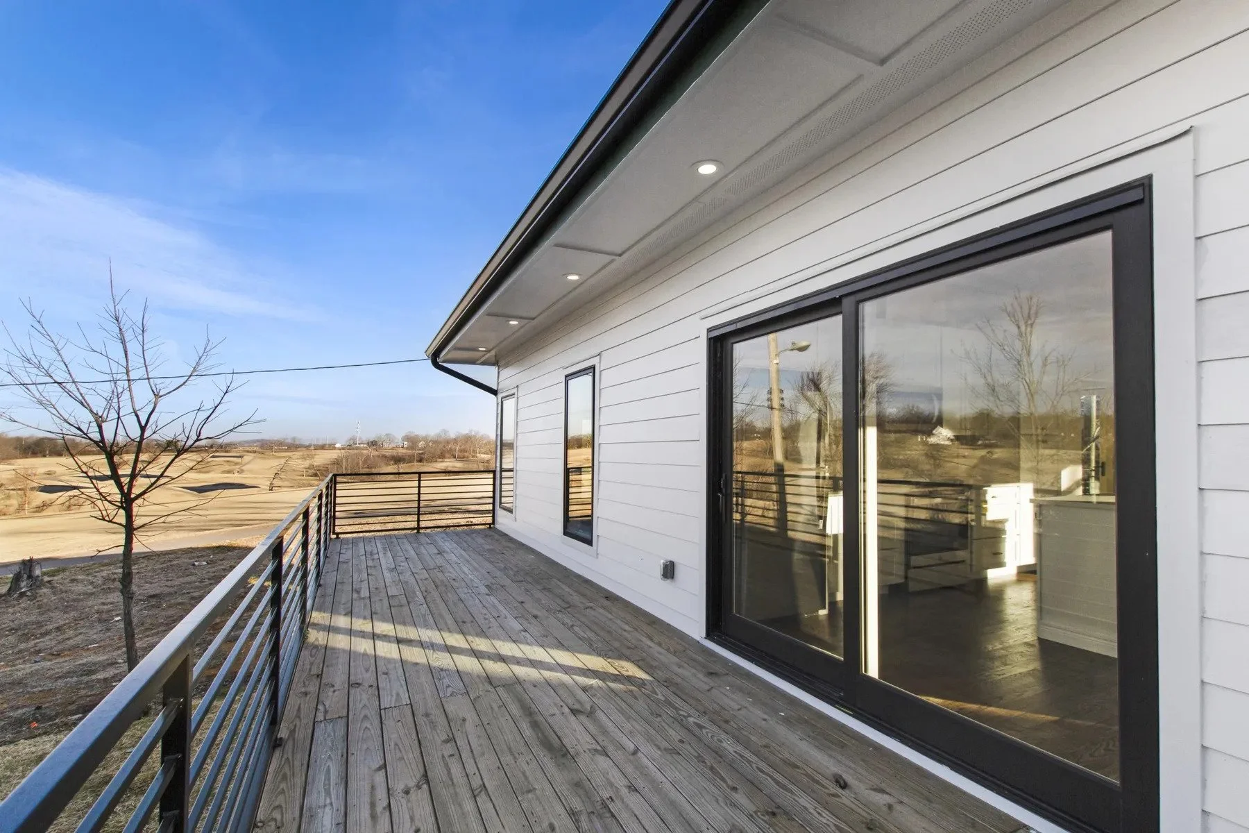Large elevated deck with black metal railing overlooking the surrounding landscape at a custom duplex home on Holly Street.