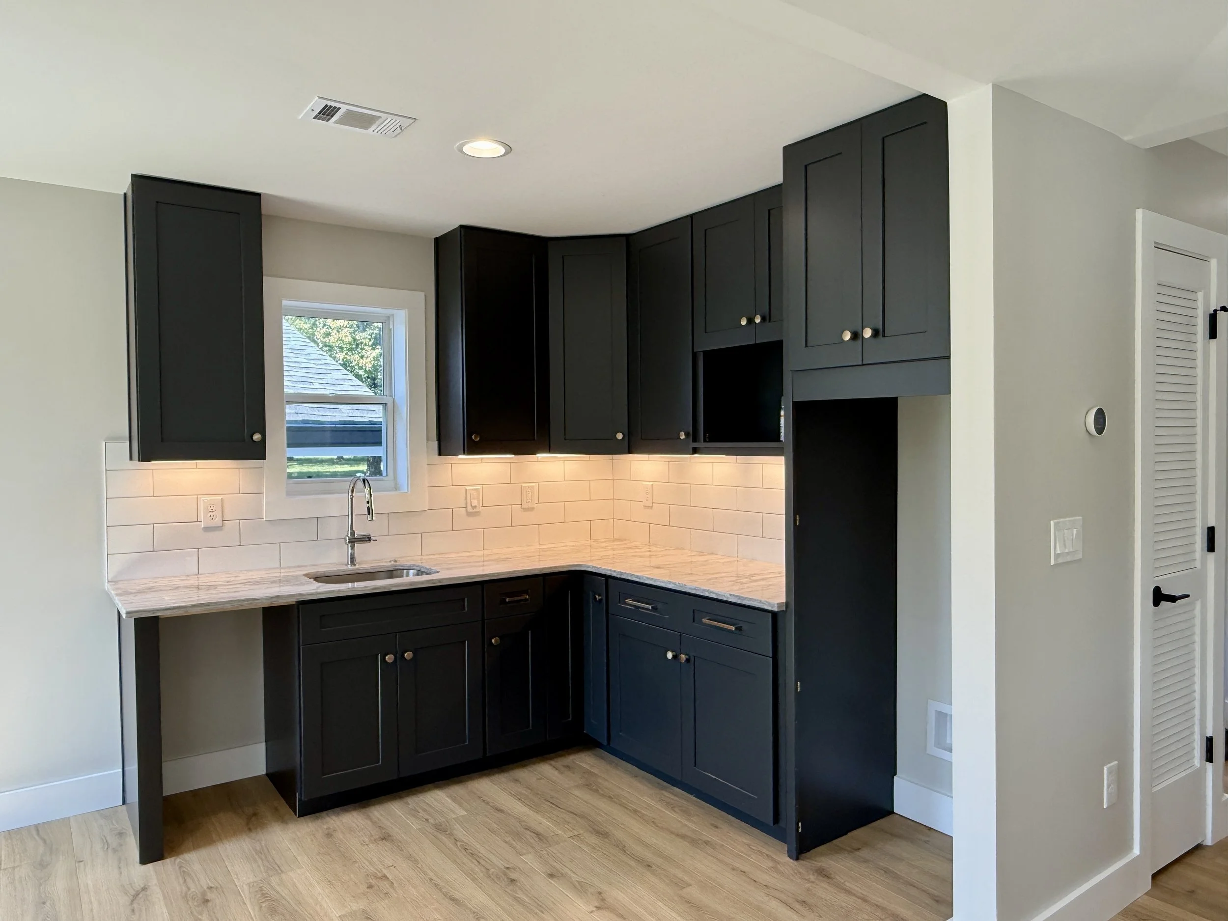 Compact kitchen with dark shaker cabinets, subway tile backsplash, and wood flooring inside a new detached accessory dwelling unit in West Meade.