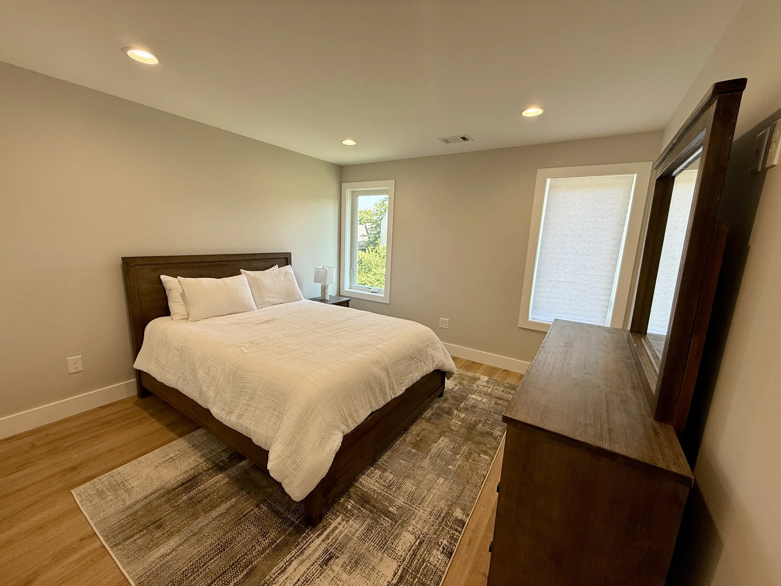 Bright bedroom with wood floors, recessed lighting, and large windows inside a detached accessory dwelling unit.
