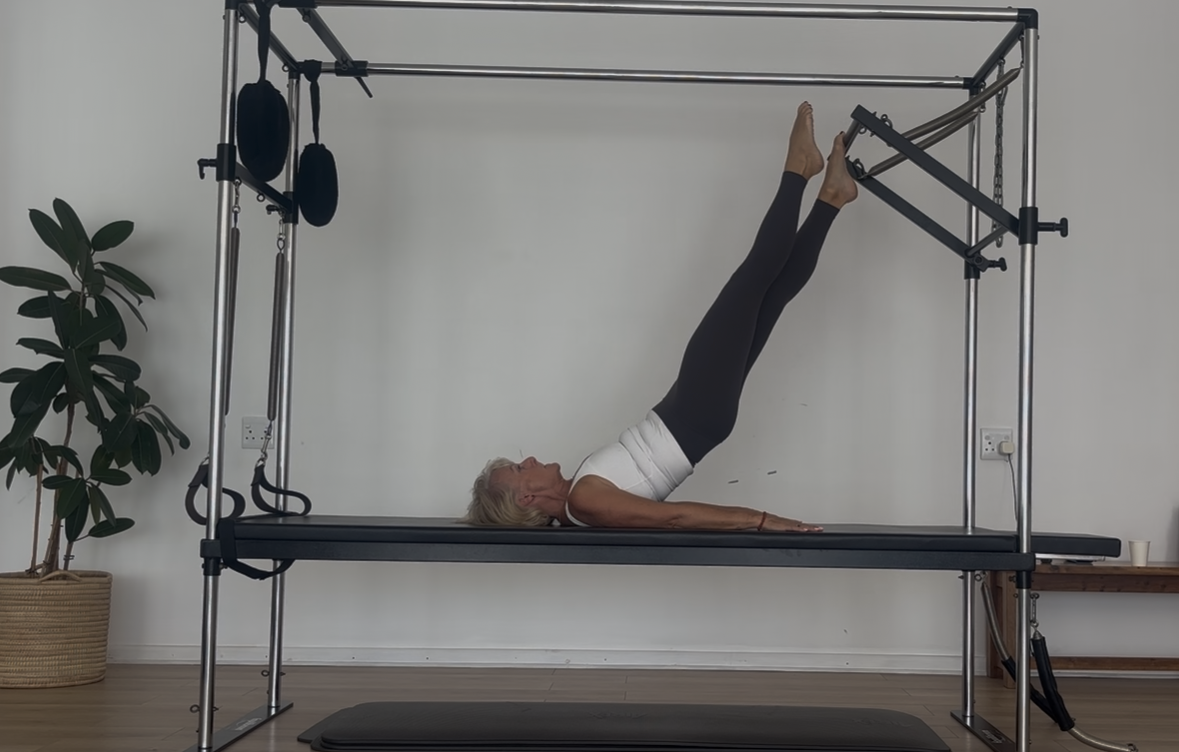 Older woman practicing pilates on a reformer machine in a home studio.