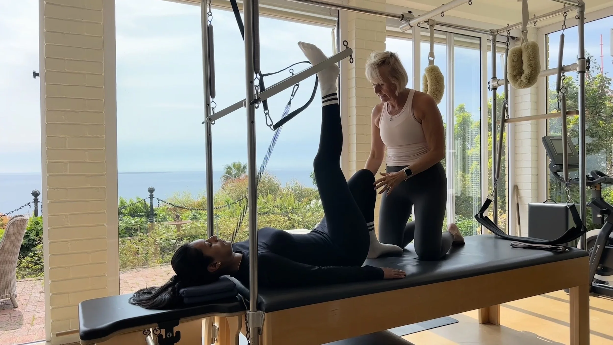Indoor physical therapy session with a therapist assisting a patient on a treatment table with a scenic ocean view in the background.