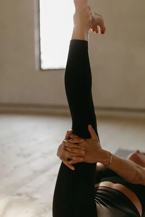 Person practicing yoga or stretching, holding one leg straight up while lying on a yoga mat indoors.