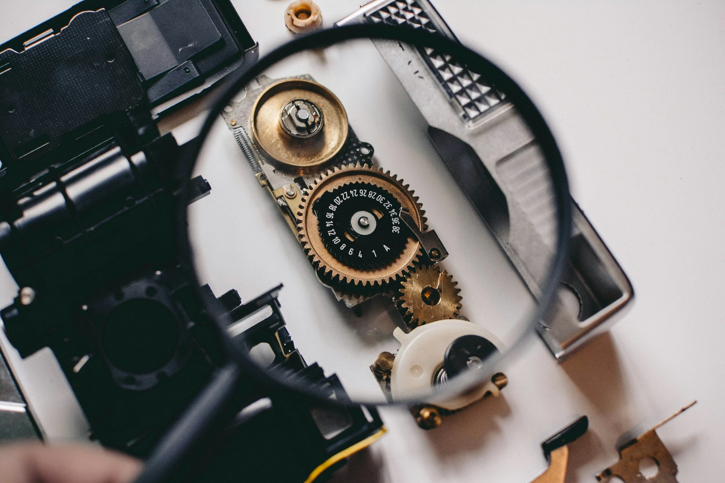 Close-up of disassembled camera with visible gears, mechanisms, and internal components on a white surface.
