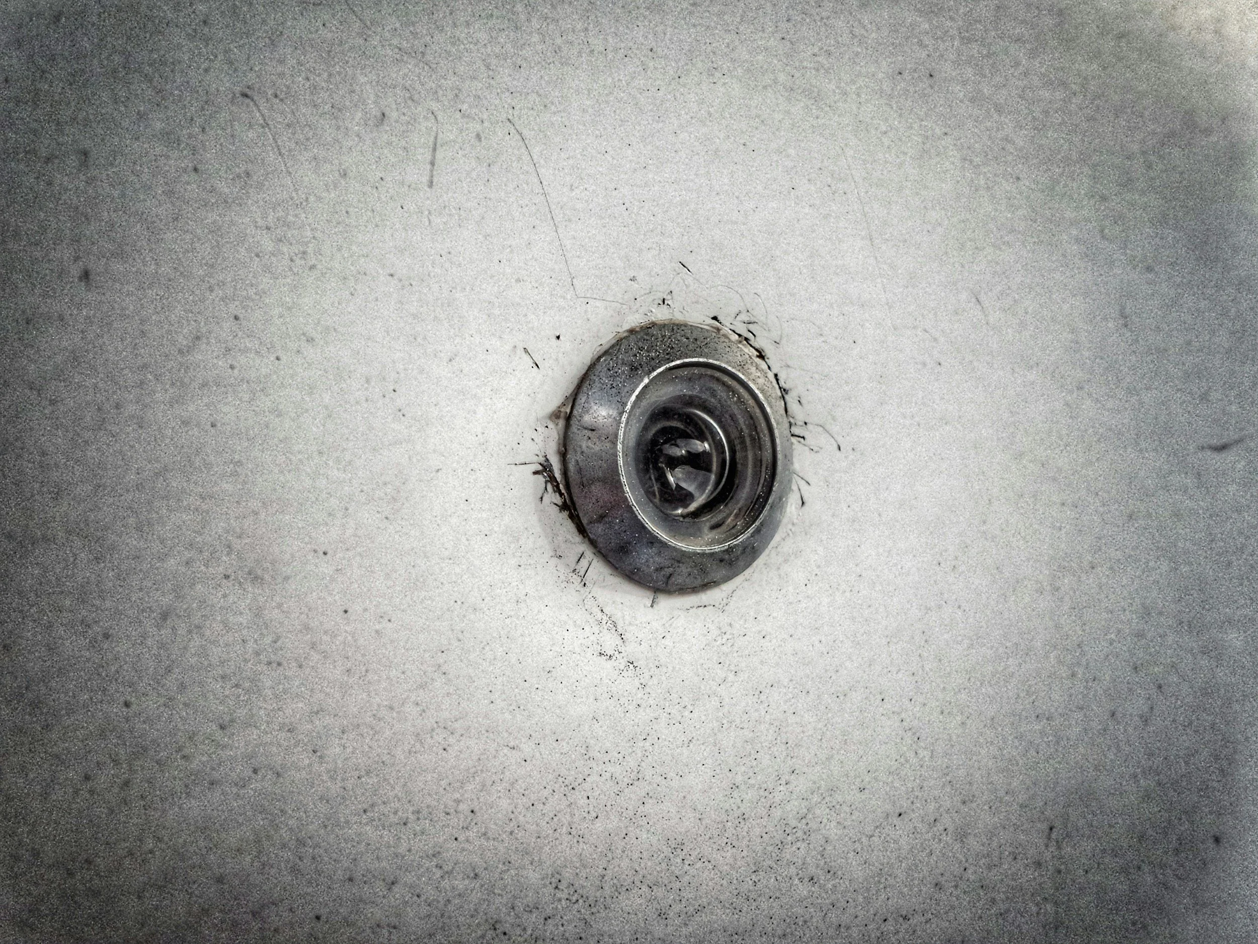 Close-up of a stainless steel drain in a light gray sink, with some dirt and debris around it.