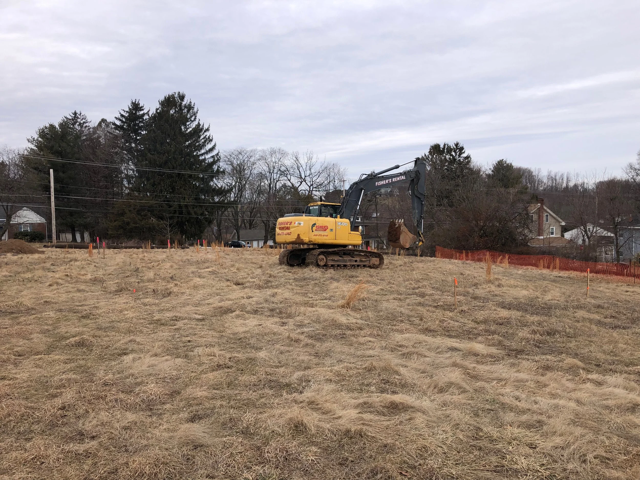 An excavator on a grassy construction site with orange fencing