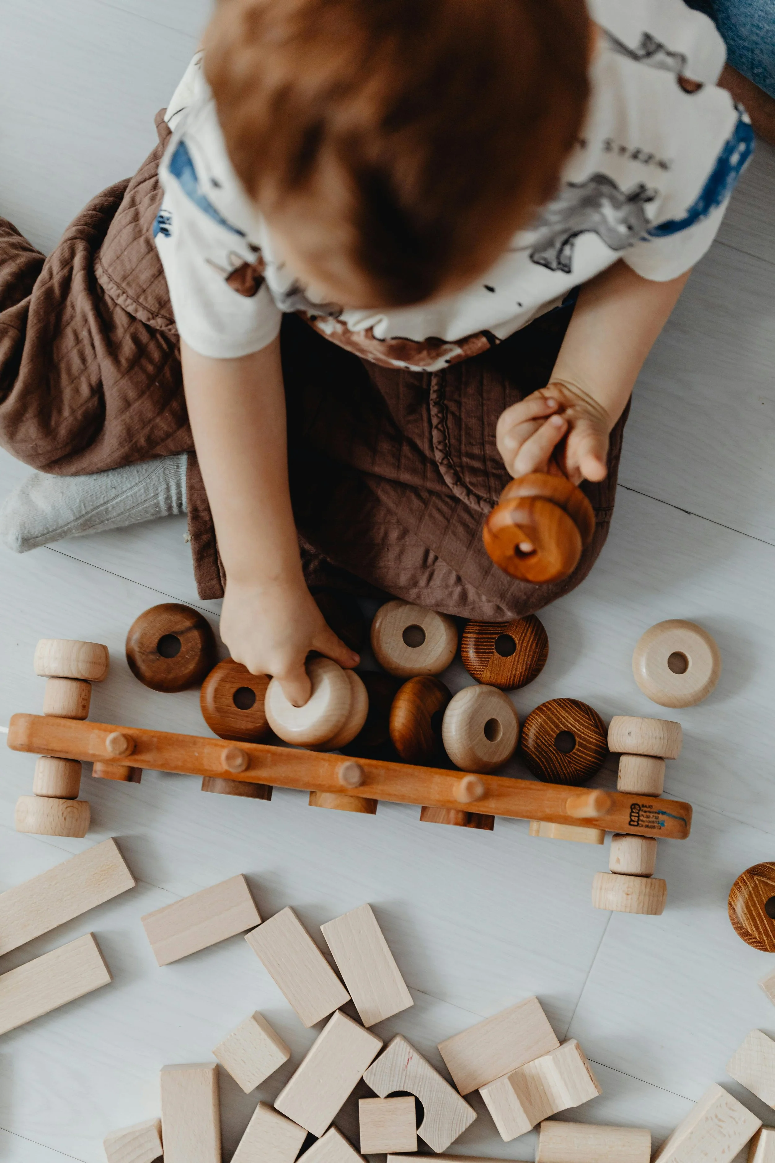 A young child sitting on the floor playing with wooden stacking toys and blocks.