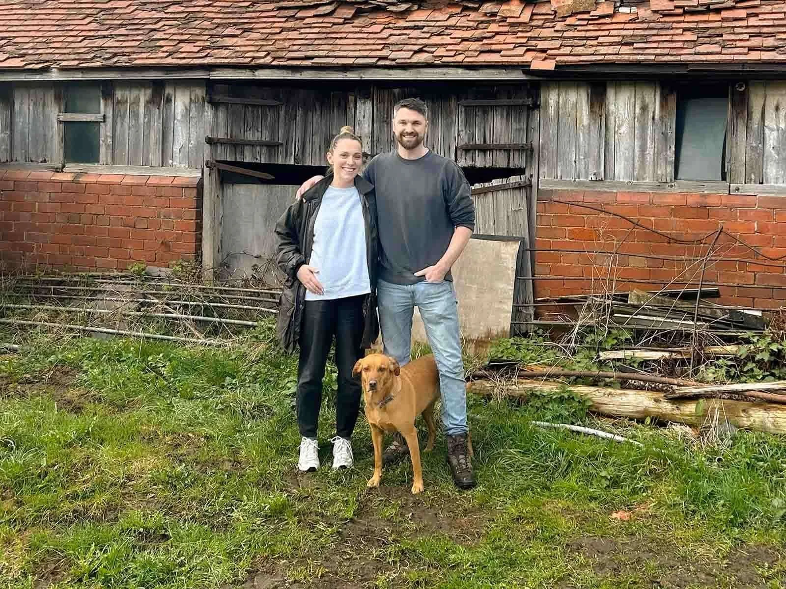 Richard and Ffion standing with their dog outside the old cow shed before its restoration into a family home.