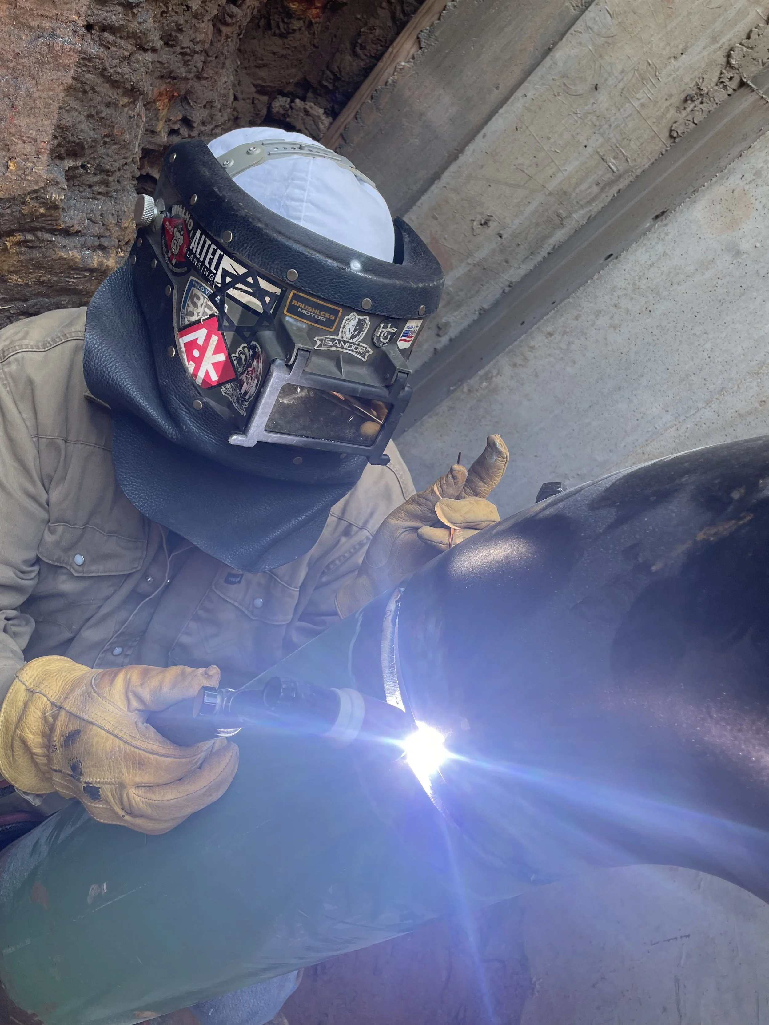 Industrial welder performing field welding on carbon steel piping.