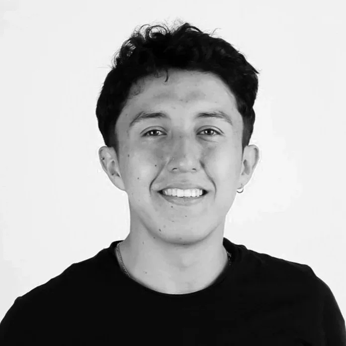 Retrato de un joven sonriendo, con cabello oscuro y short estilo casual, en blanco y negro.