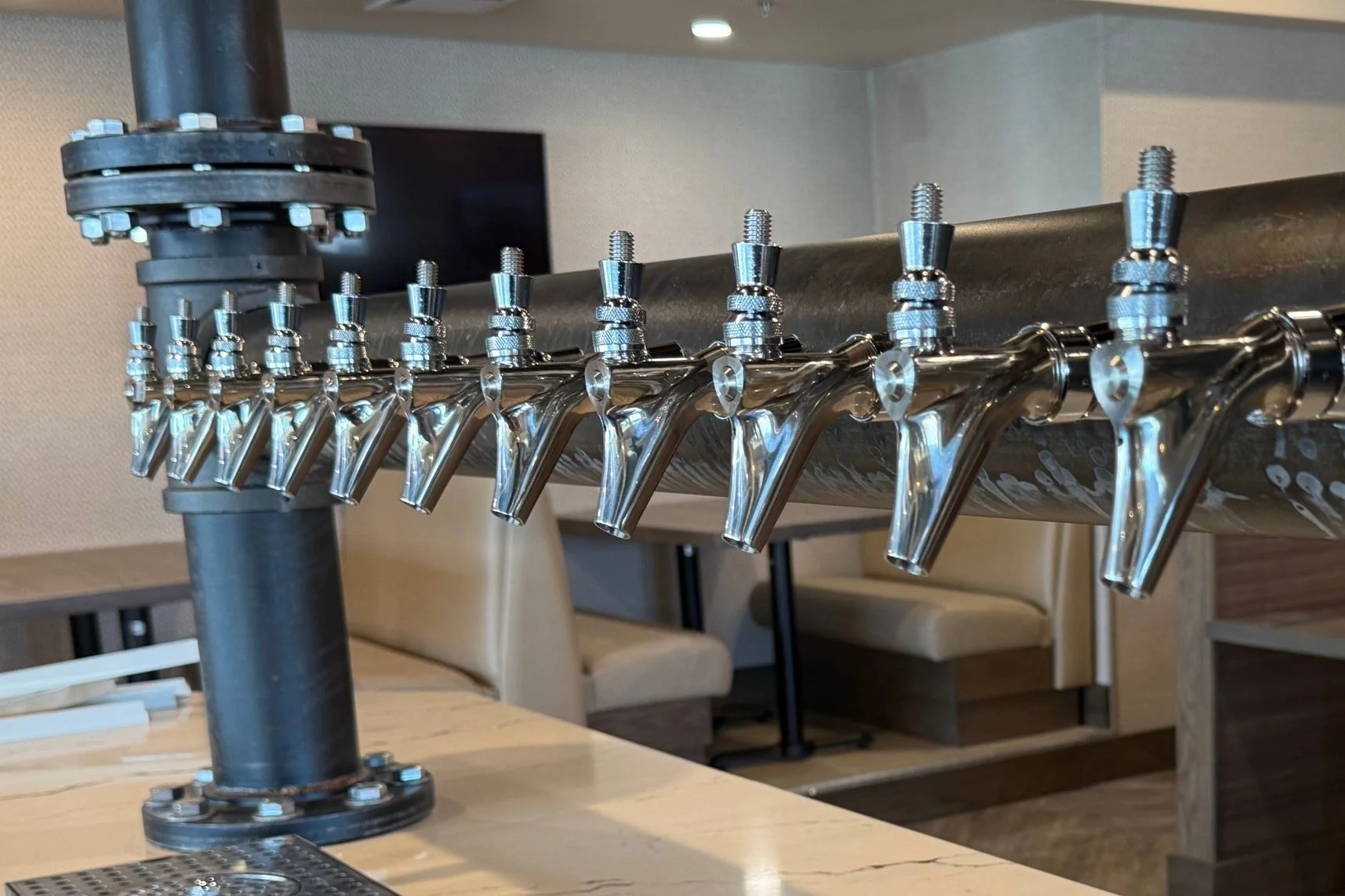 Row of shiny metal beer taps on a bar counter in a restaurant.