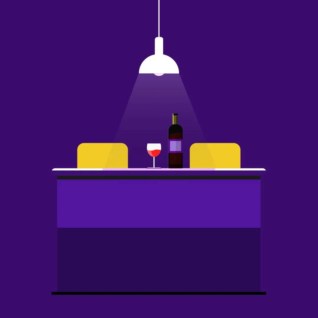A wine bottle, a glass of red wine, and yellow chairs on a table under a hanging white lamp in a dark purple room.