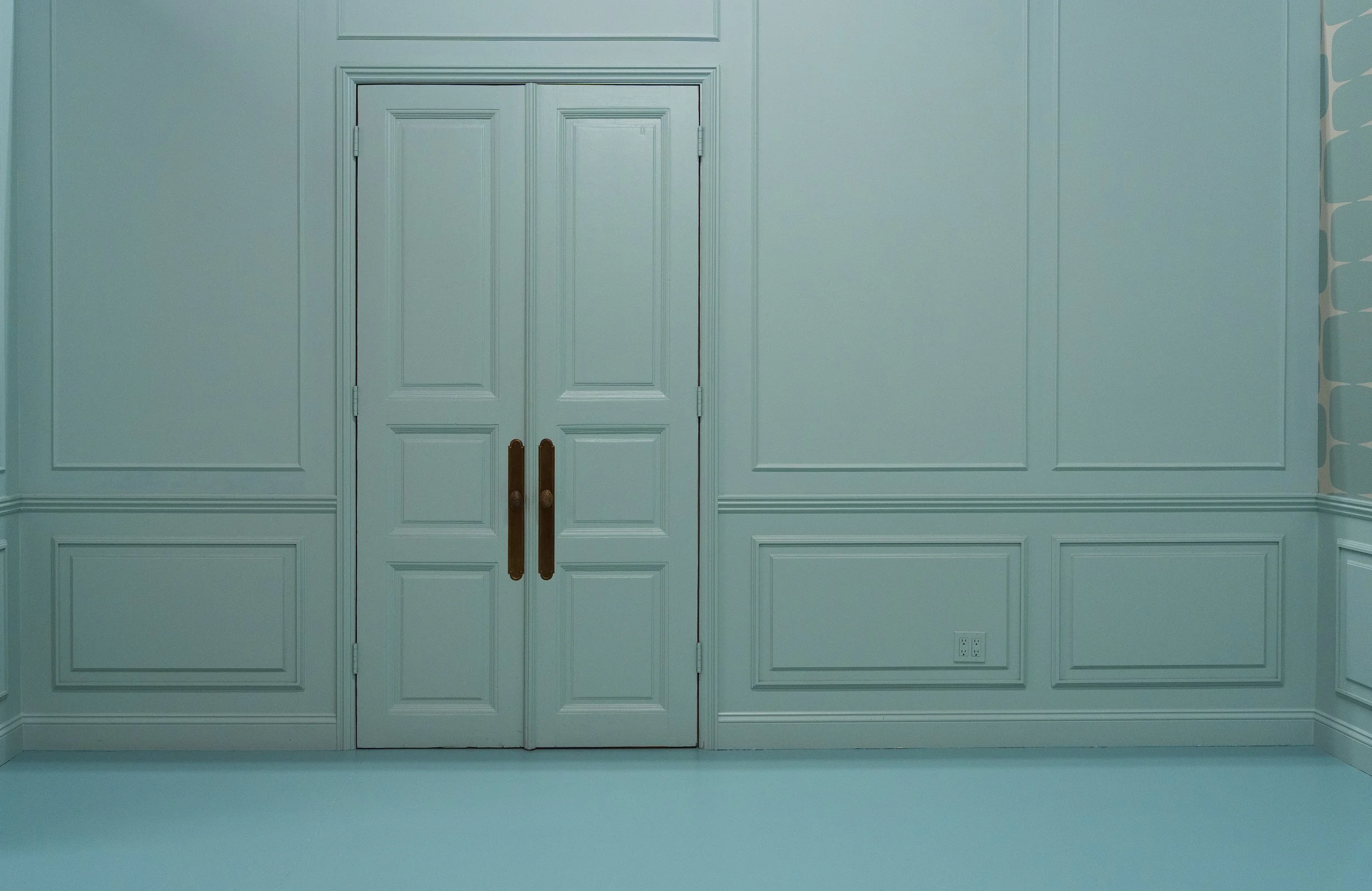 White double doors with gold handles set in a room with pale blue walls and decorative molding.