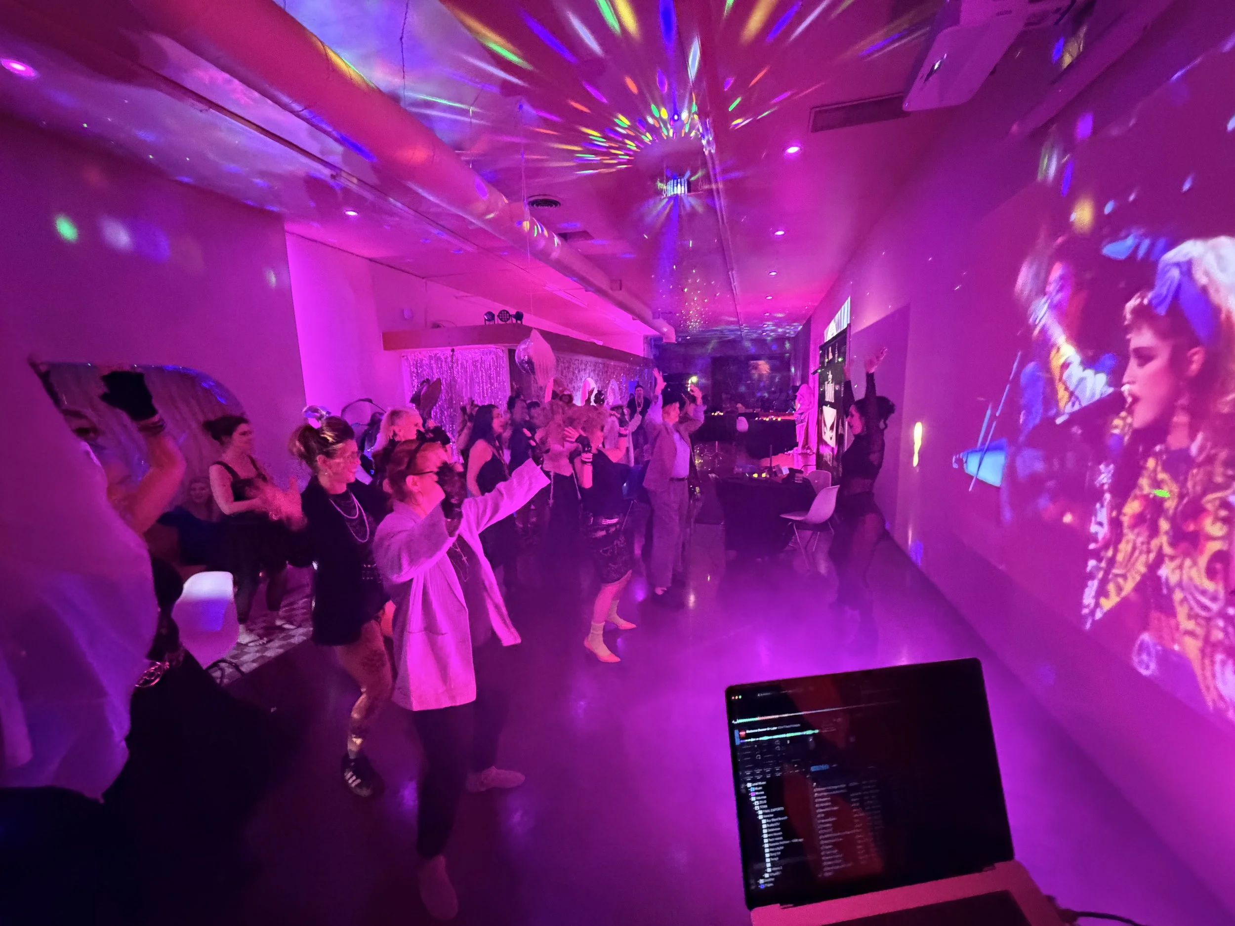 People dancing at a party with colorful disco lights on the ceiling and walls.