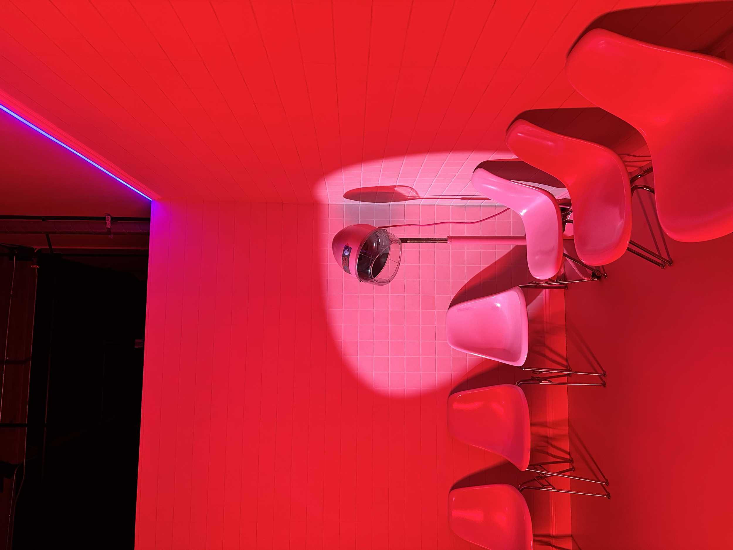 A room with red illuminated walls, ceiling, and furniture, including four red chairs and a hairdryer on a stand.