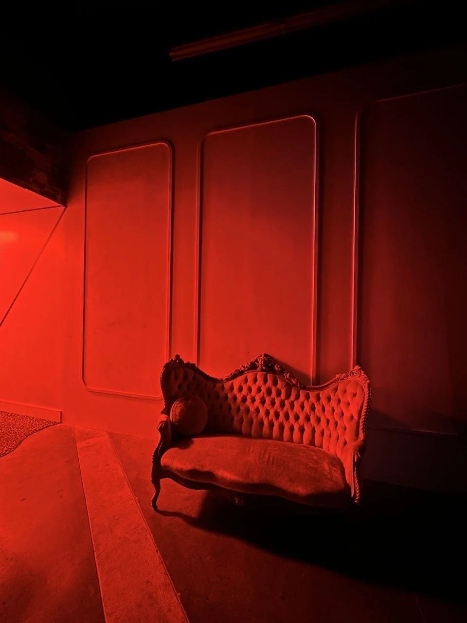A vintage-style red velvet tufted sofa in a dimly lit room with red lighting and modern wall panels.