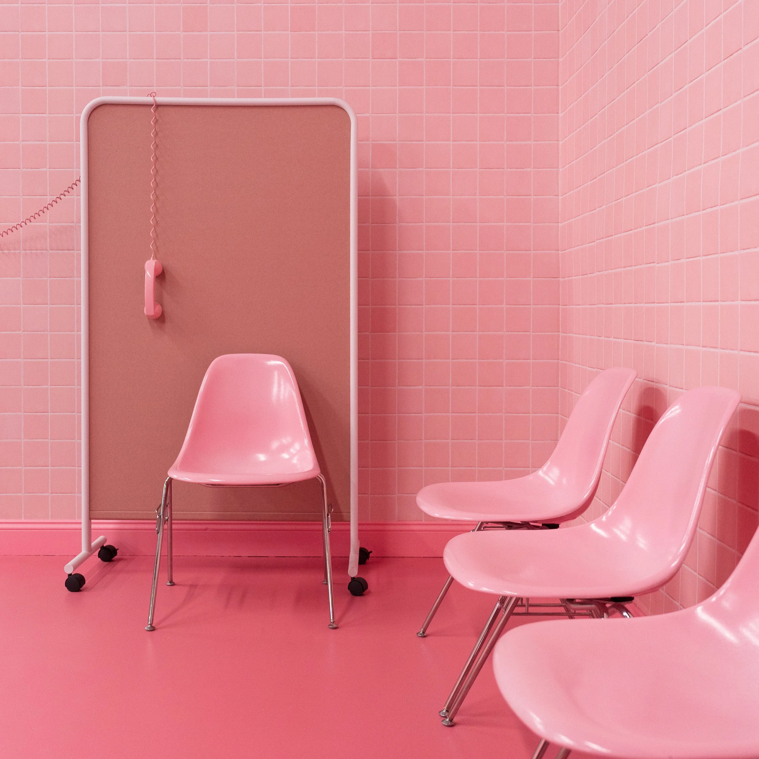 A retro living room with a yellow sofa, pink and green floor tiles, a vintage TV, and leopard print wallpaper. Decor includes a blue bust, pink rotary phone, colorful lamp, and geometric rug.
