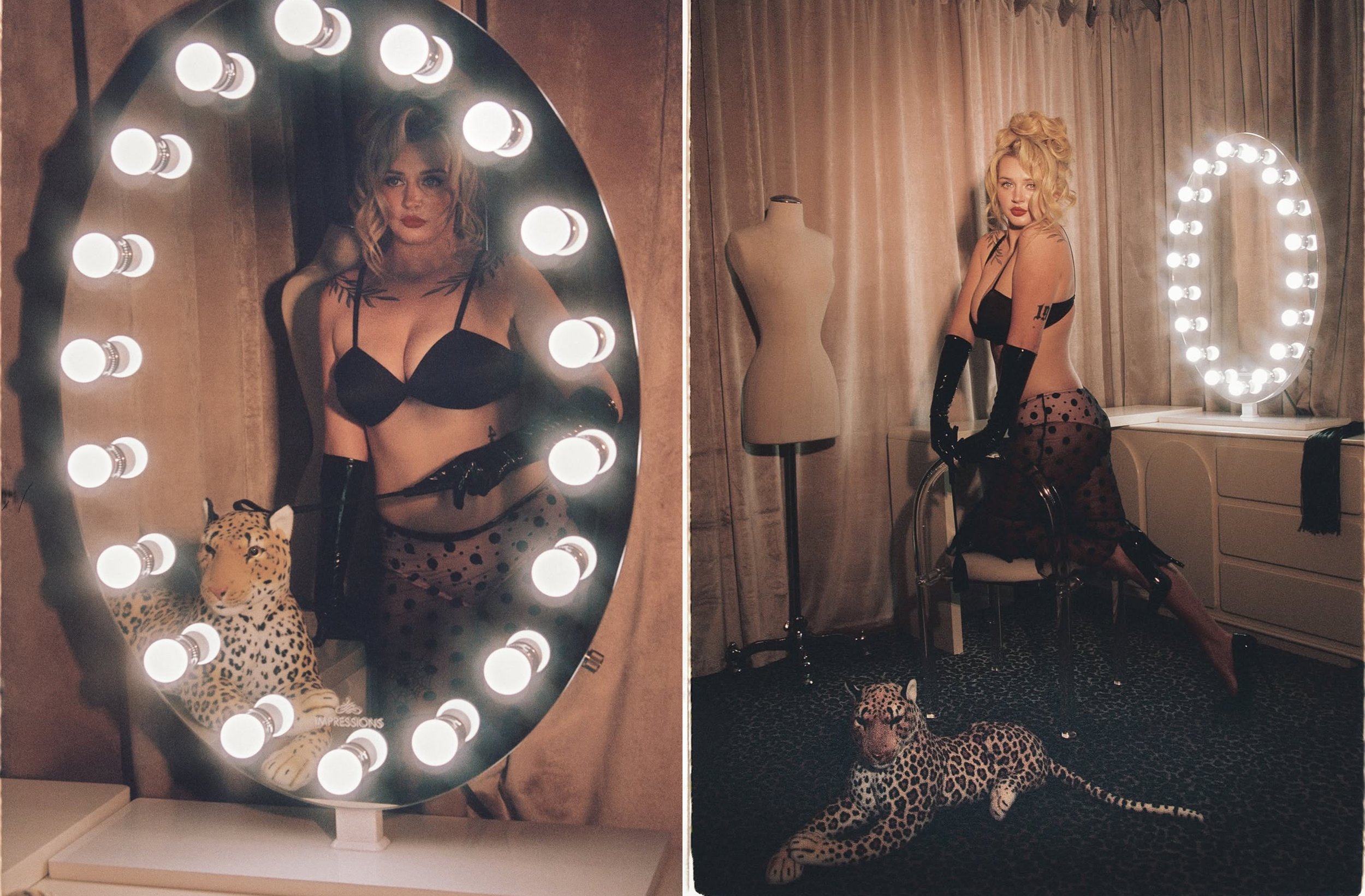 A woman with blonde curly hair and tattoos wearing black lingerie and gloves, posing in front of a mirror with light bulbs, in a room with curtains and a mannequin, with a leopard plush at her feet.