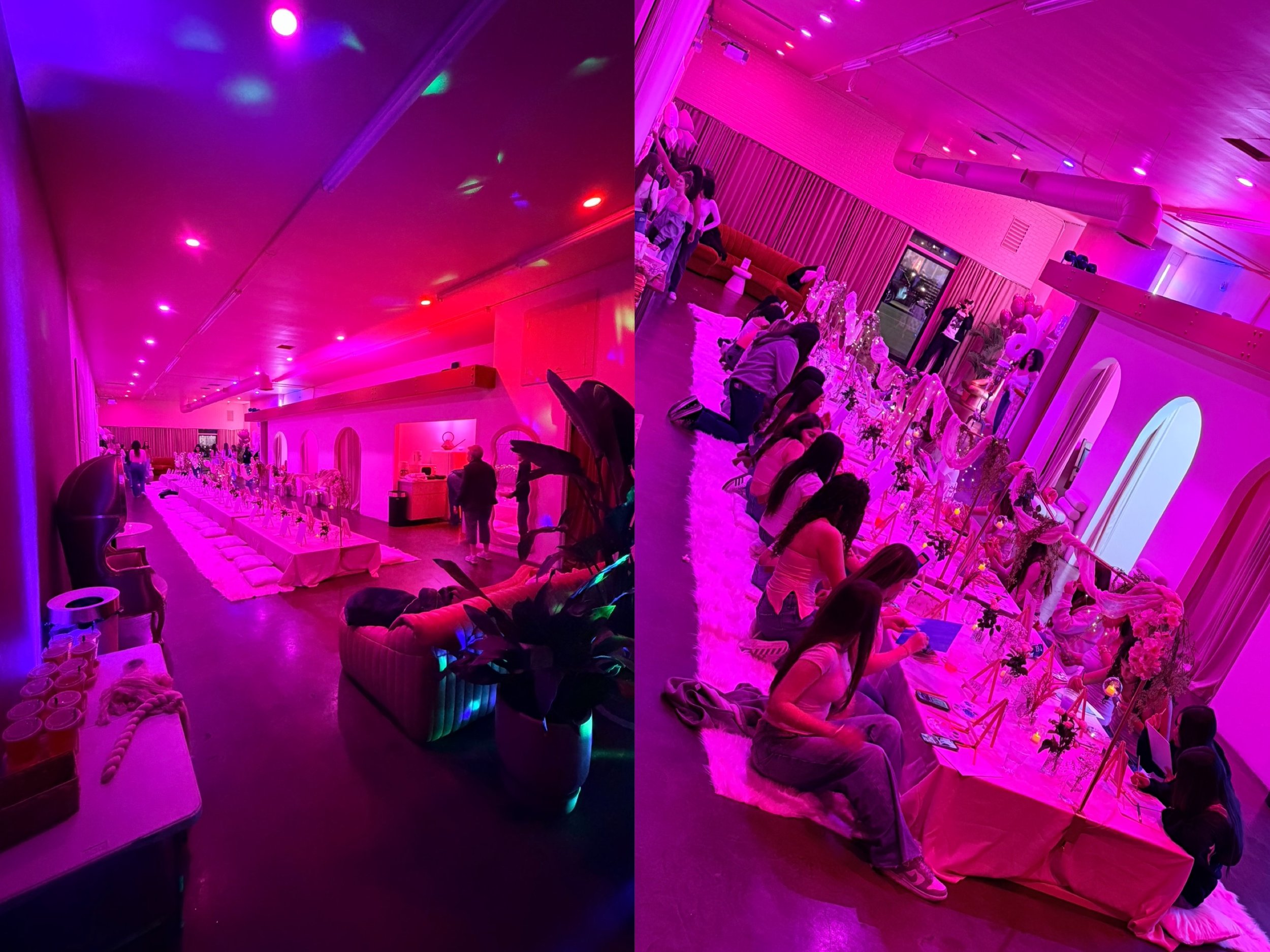Party room decorated with pink and purple lighting, featuring a long table with flower arrangements and people sitting and kneeling around it, creating a festive atmosphere.