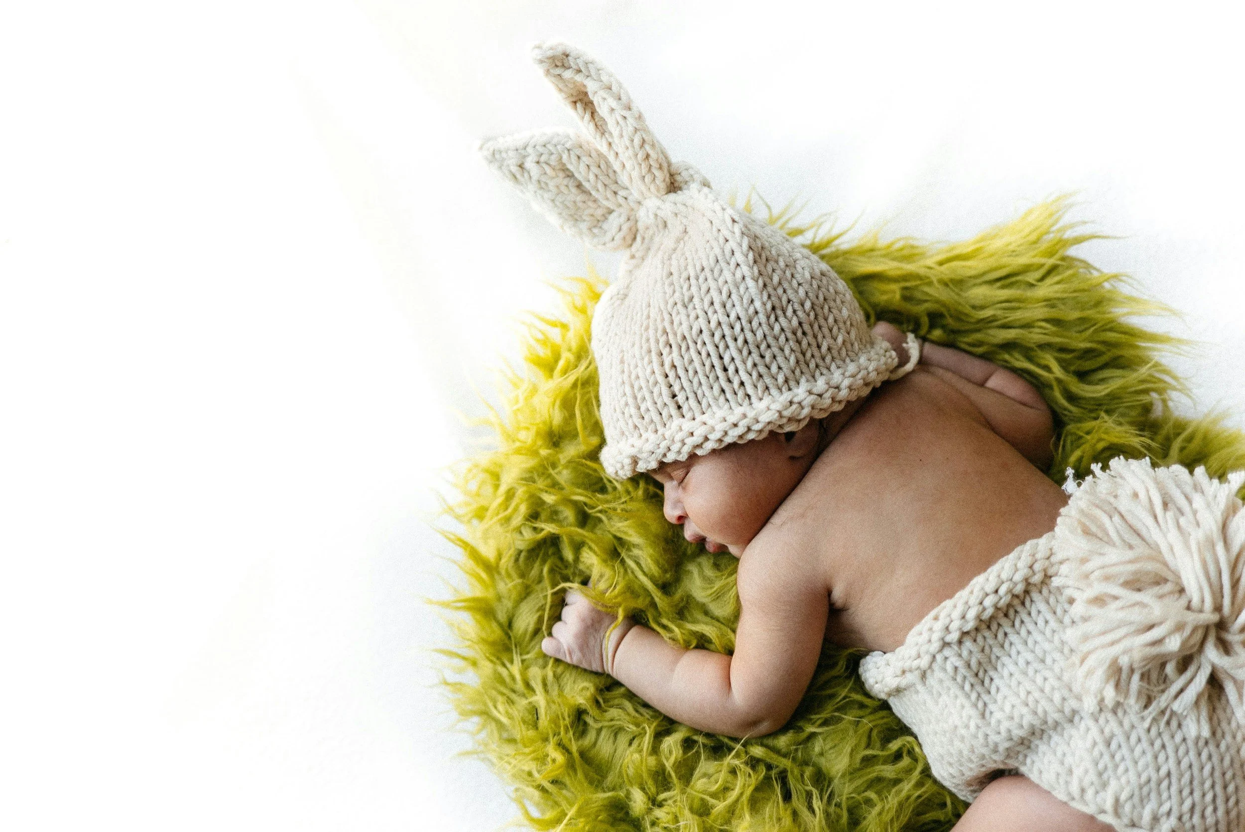 A sleeping baby with a beige knitted hat with bunny ears, lying on bright yellow furry blanket.