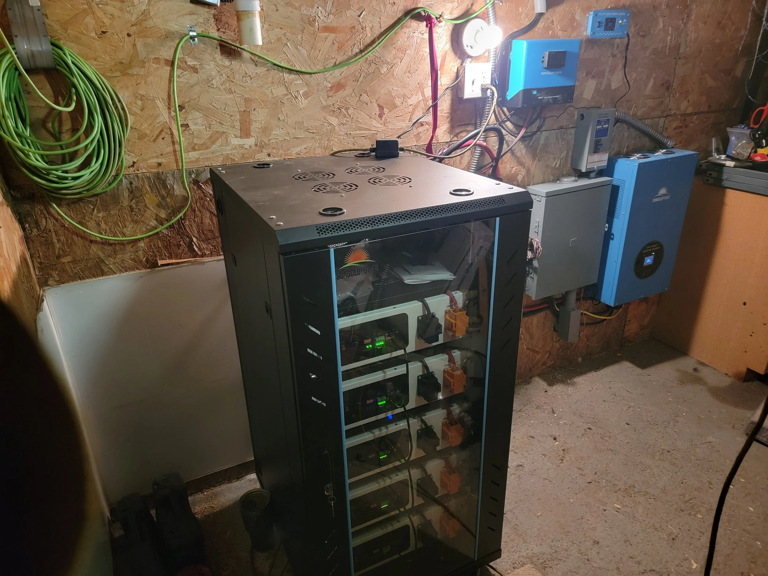 A server rack with multiple power supplies and electronic components in a workshop with wood-paneled walls and exposed wiring.