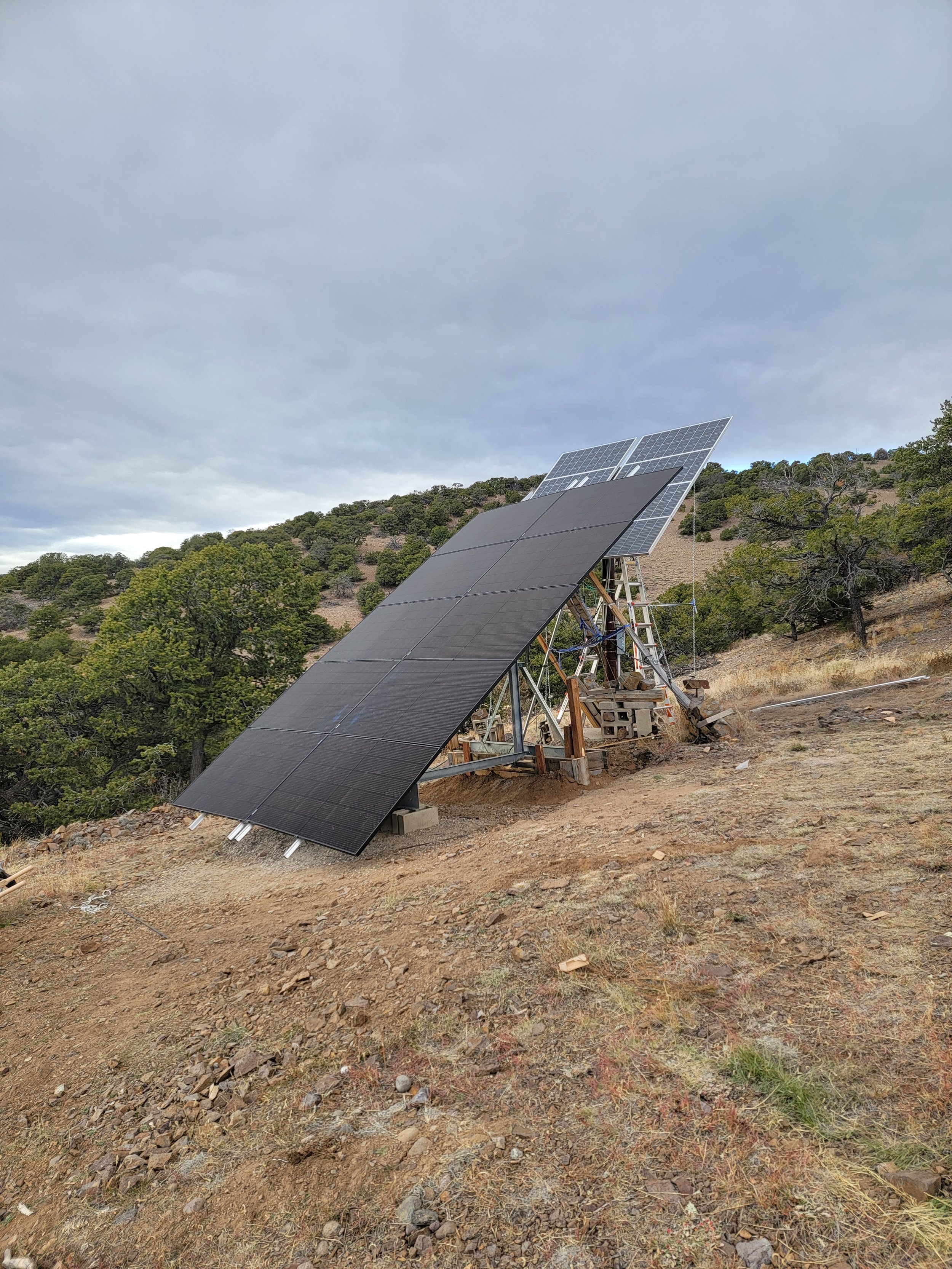 Solar panels installation on a hillside with cloudy sky and sparse vegetation.