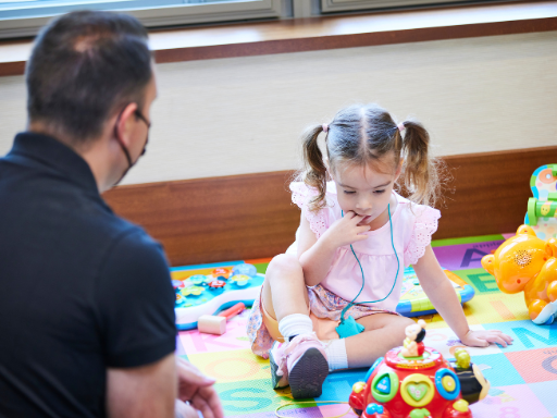 A young girl plays on a mat while her father watches