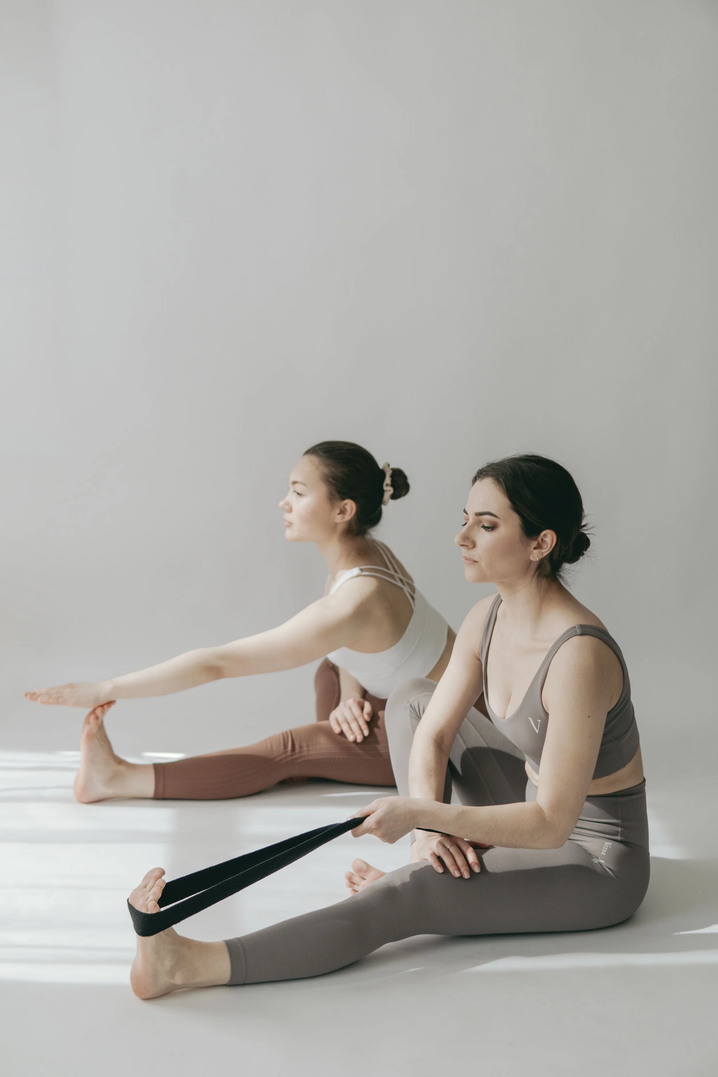 two women doing seated single leg stretch with strap